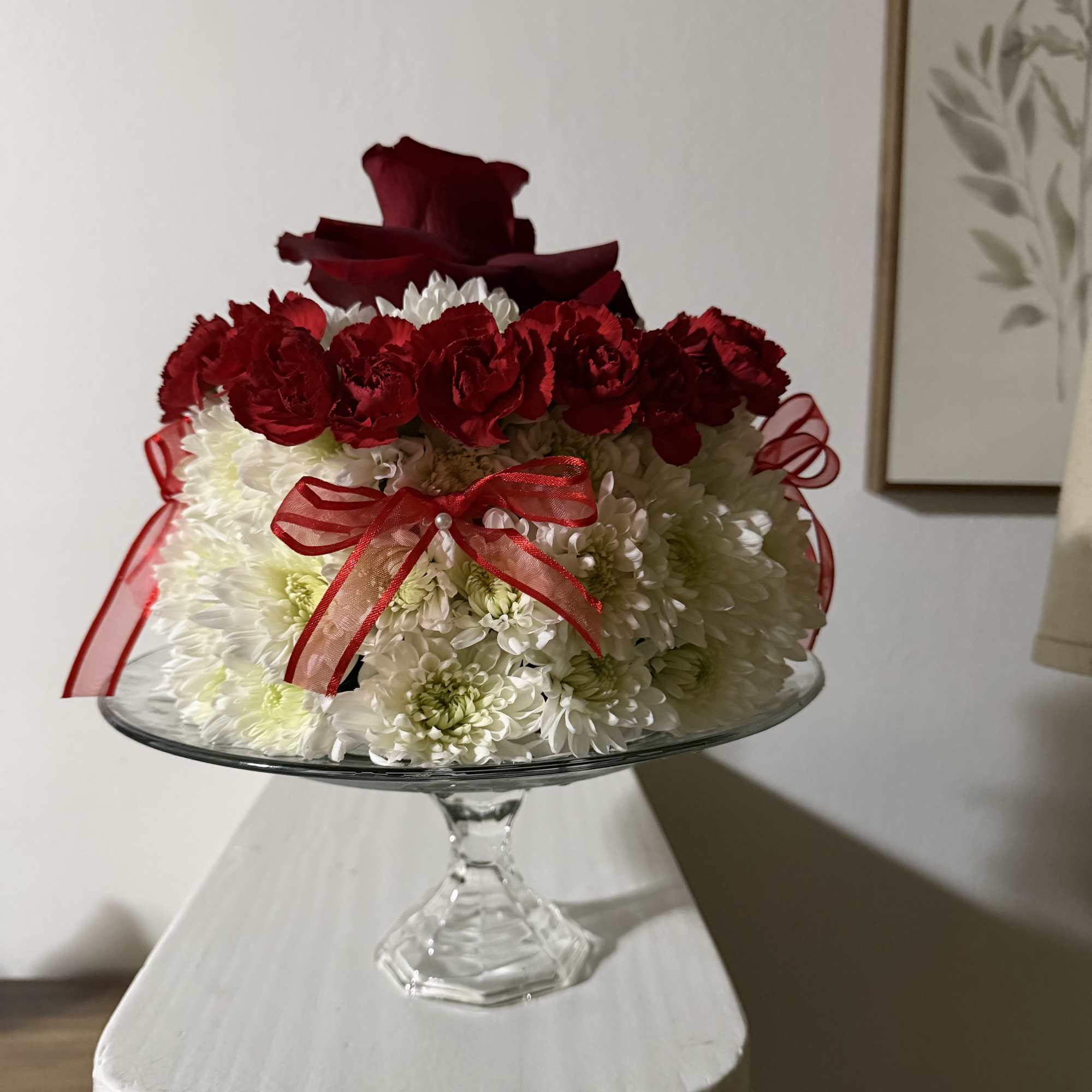 Red and white floral arrangement in a glass pedestal bowl with ribbon