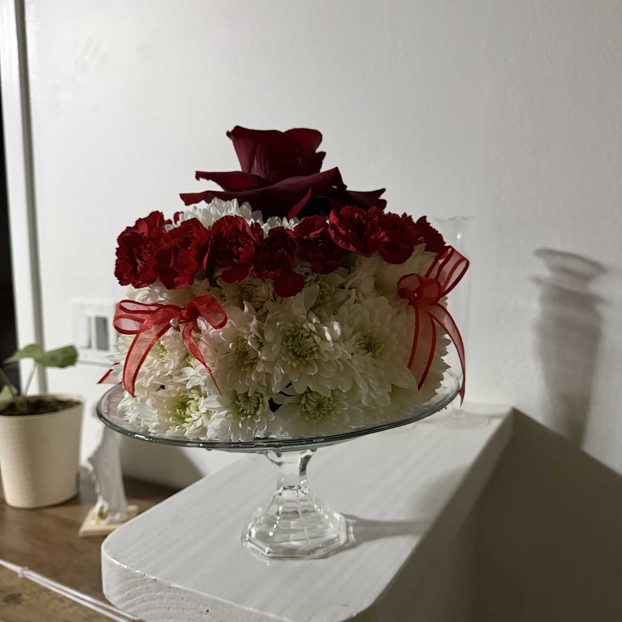 Red roses and white chrysanthemums arranged in a glass pedestal bowl