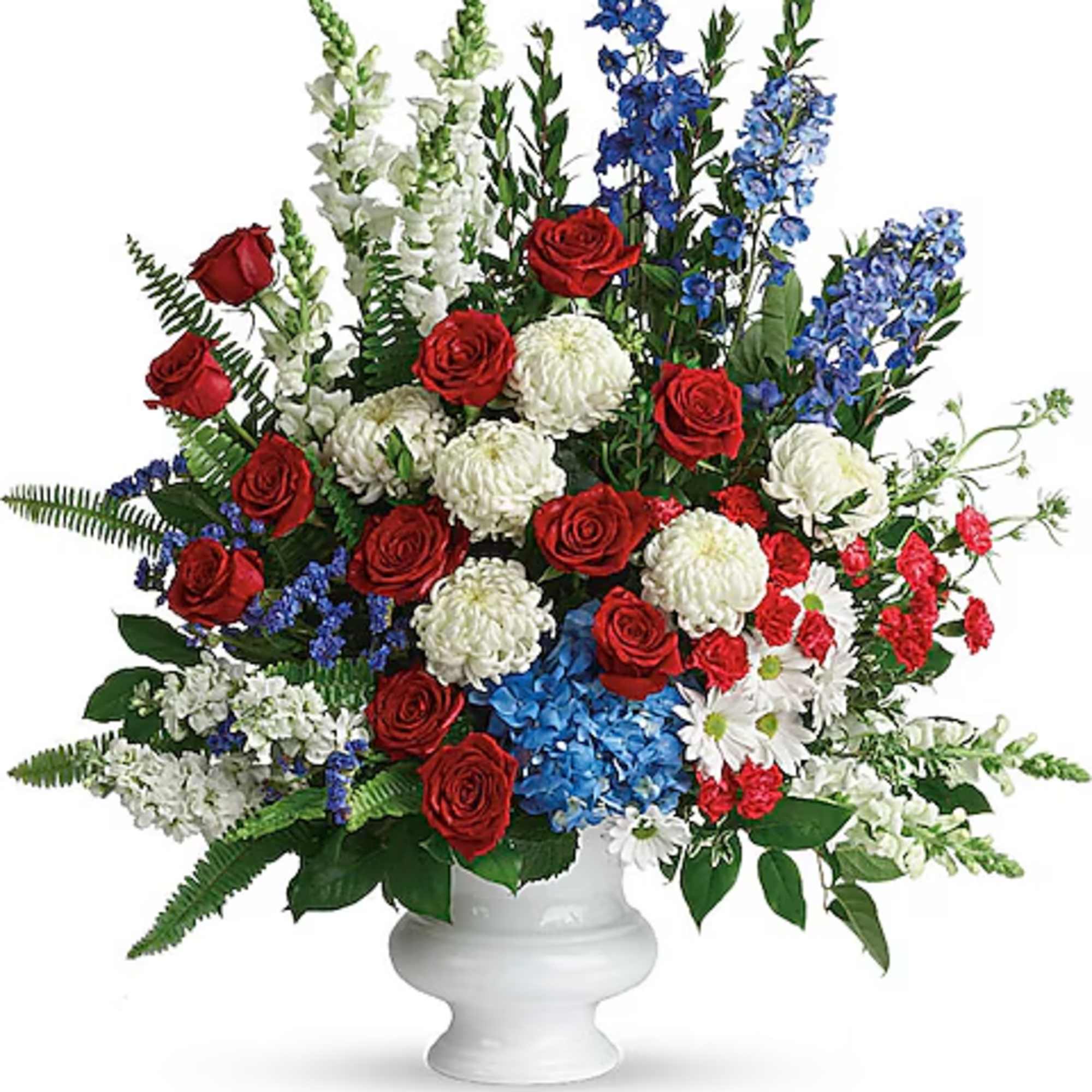 Red roses, white mums, and blue flowers arranged in a white pedestal vase