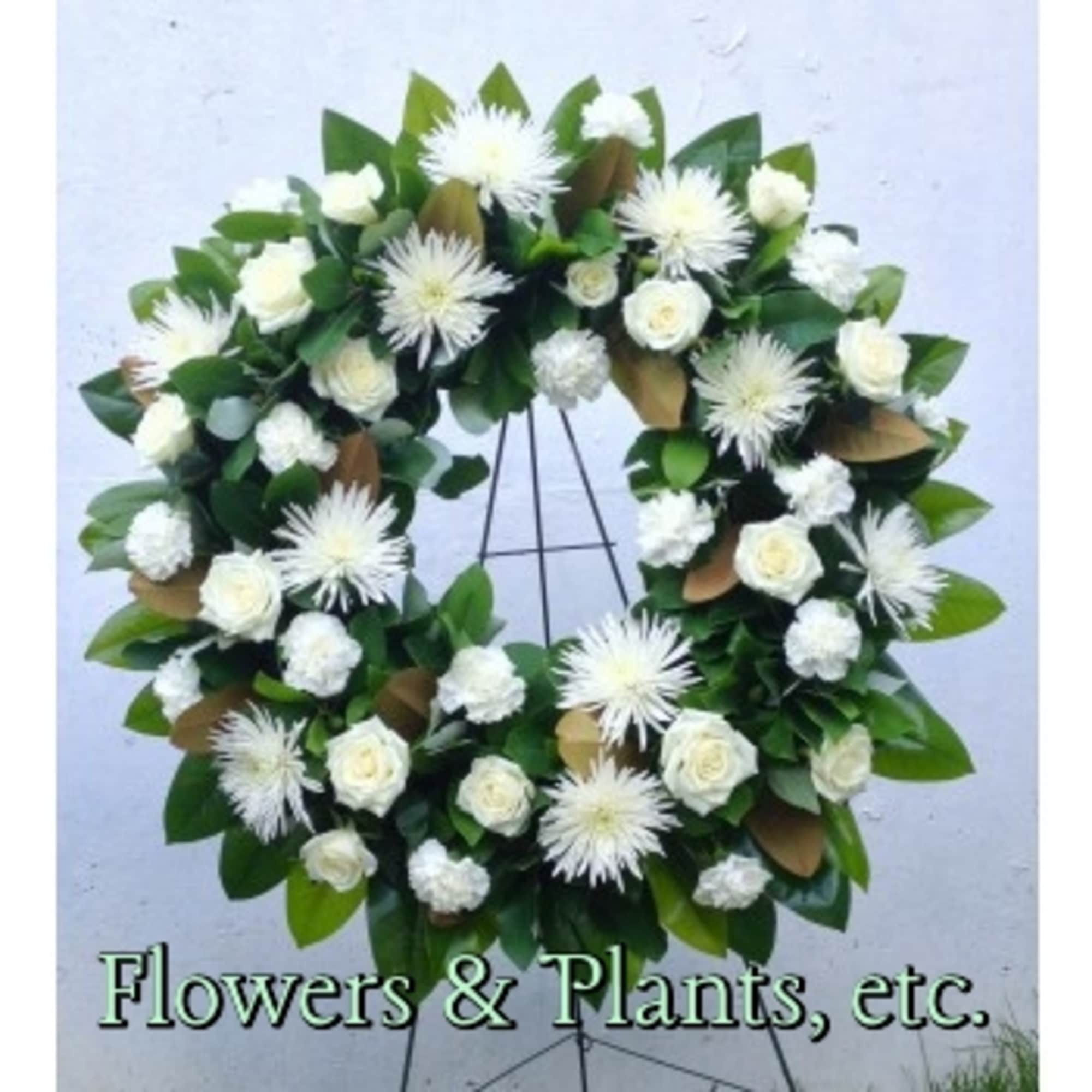 White floral wreath on a metal stand with roses and spiky blooms