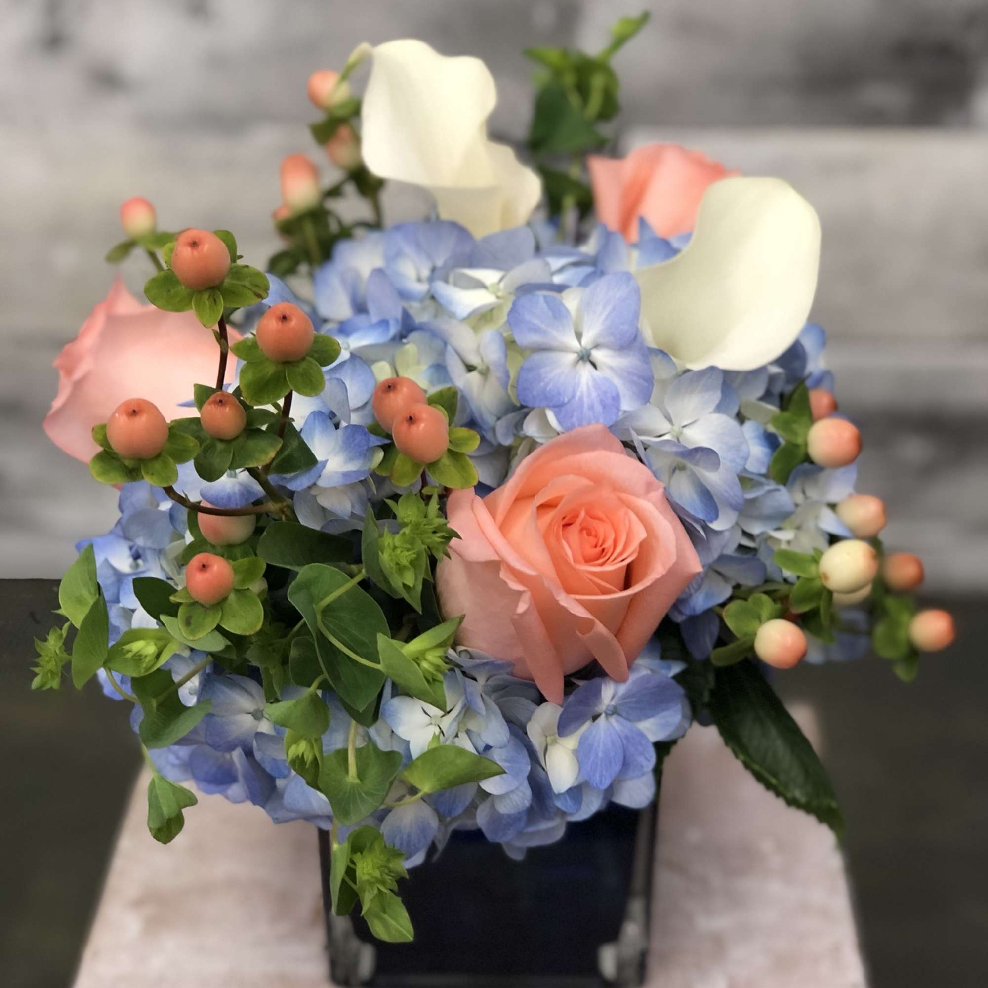Pink rose and blue hydrangea arrangement with white calla lilies in a black vase