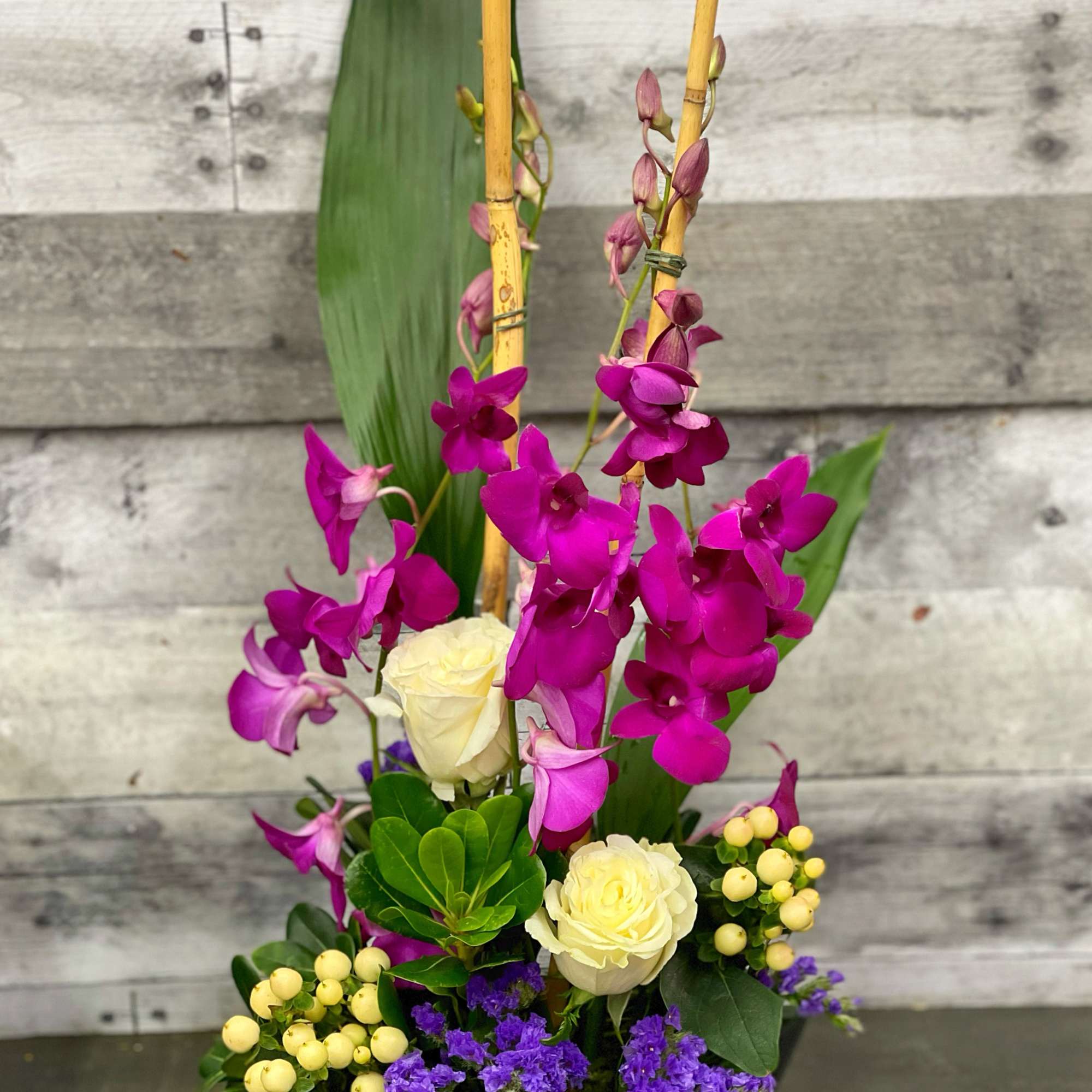 Tall floral arrangement with purple orchids and cream roses in a black container