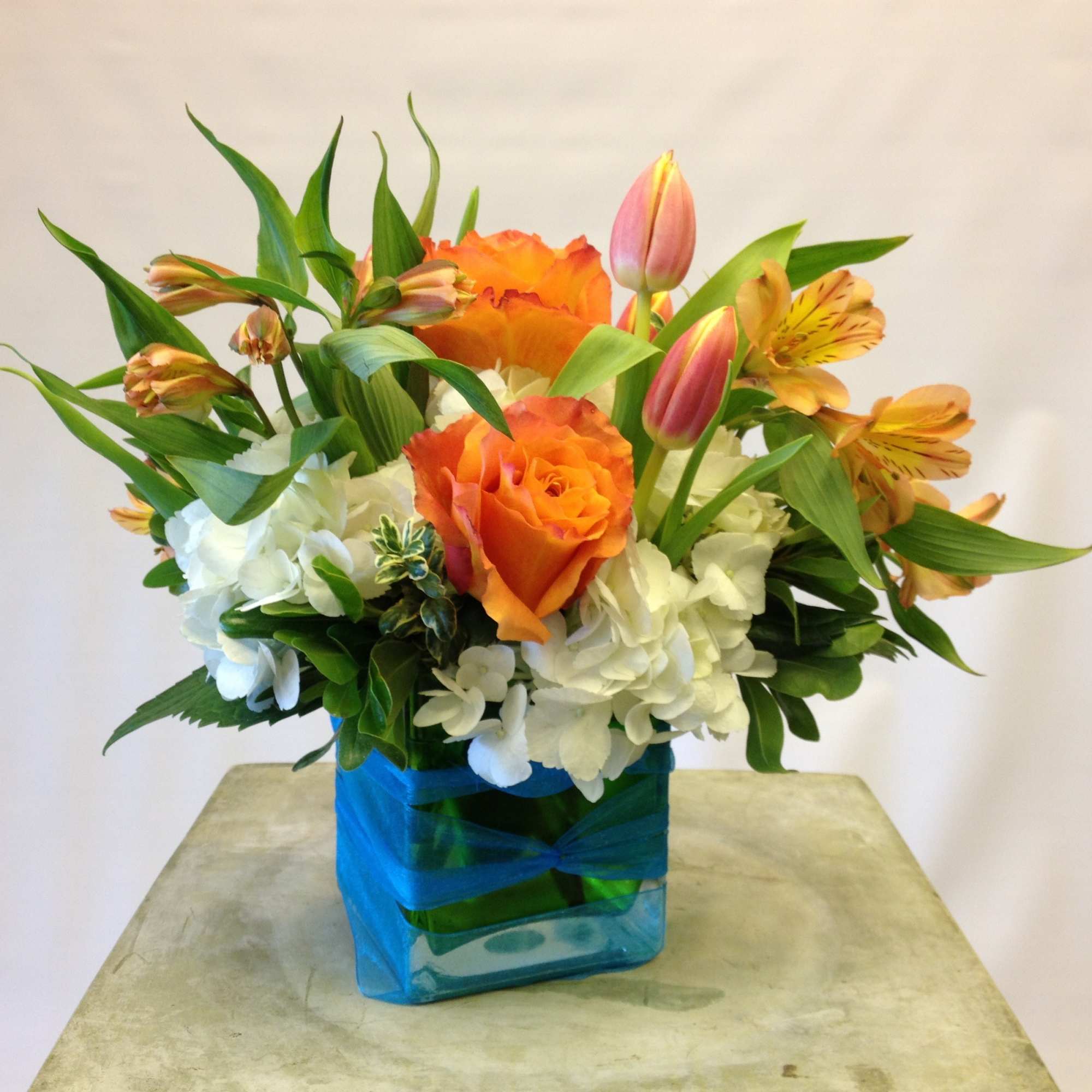 Orange roses and pink tulips in a blue glass vase