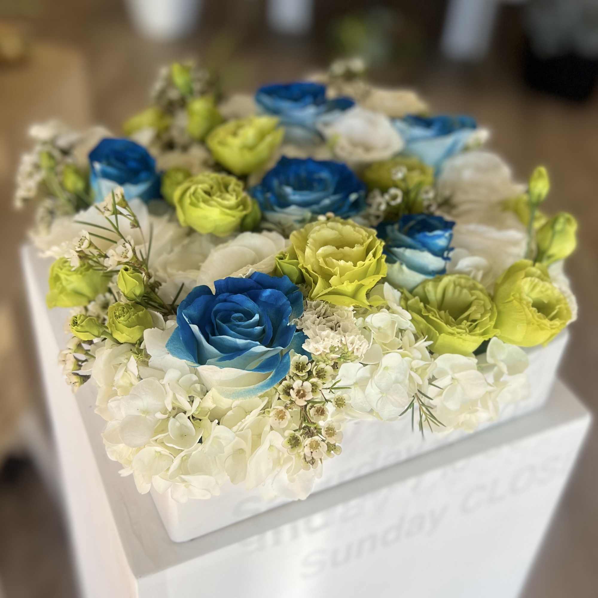 Box arrangement of blue and lime roses with white hydrangeas
