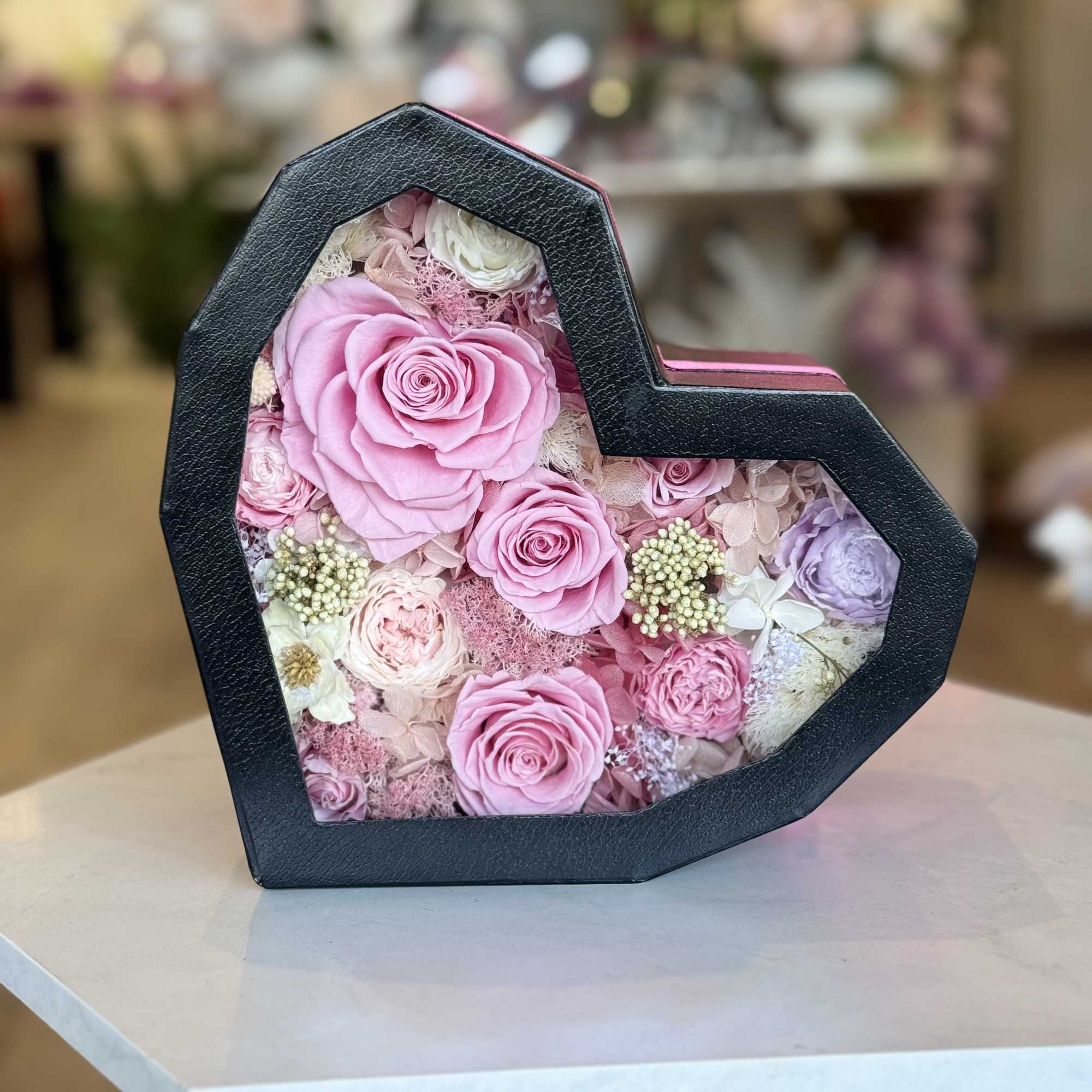A heart-shaped black gift box reveals a keepsake of preserved roses and