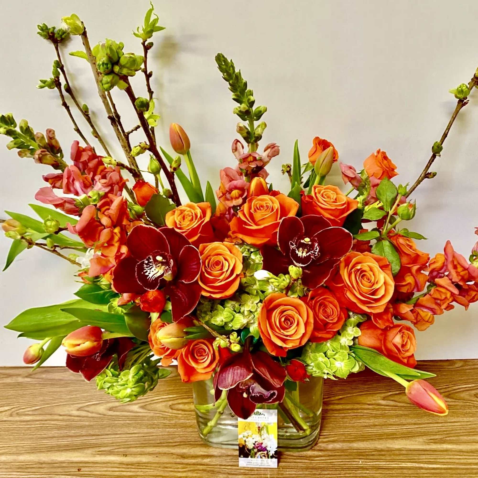 Orange roses and burgundy orchids in a clear glass vase