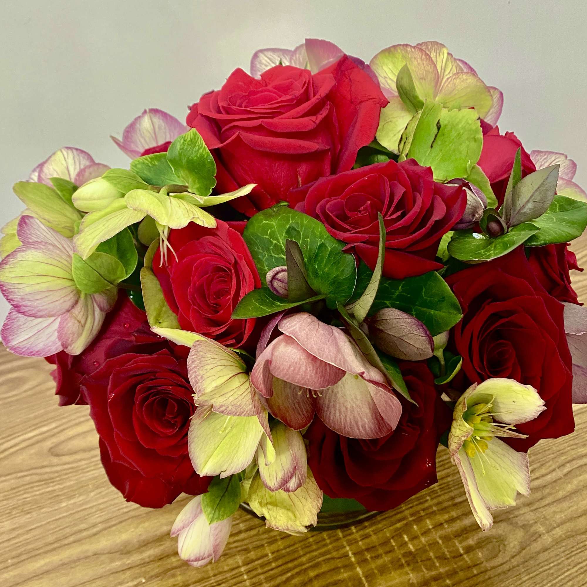 Red roses with pale green and pink hellebore flowers in a low bouquet