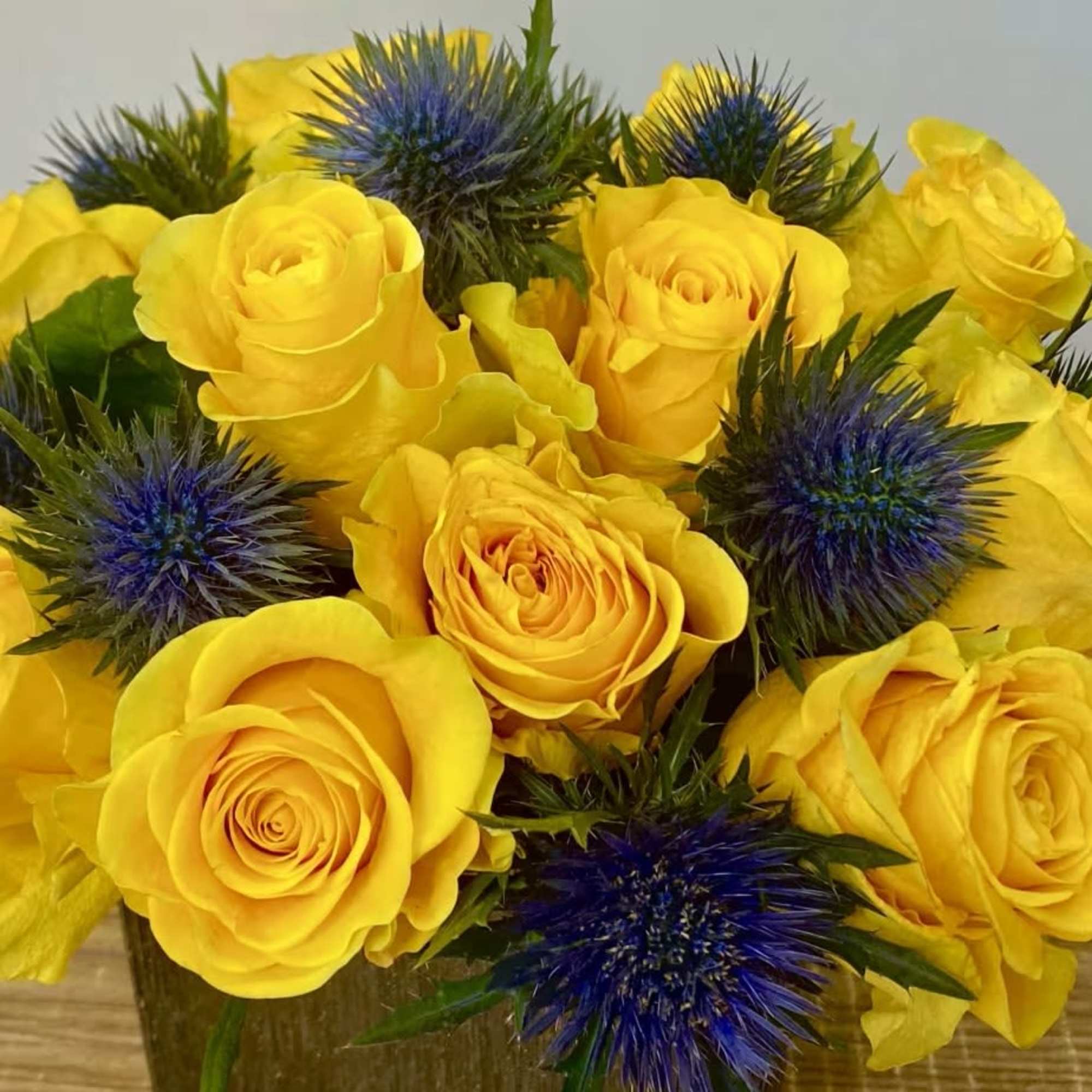 Yellow roses with blue thistle in a vase
