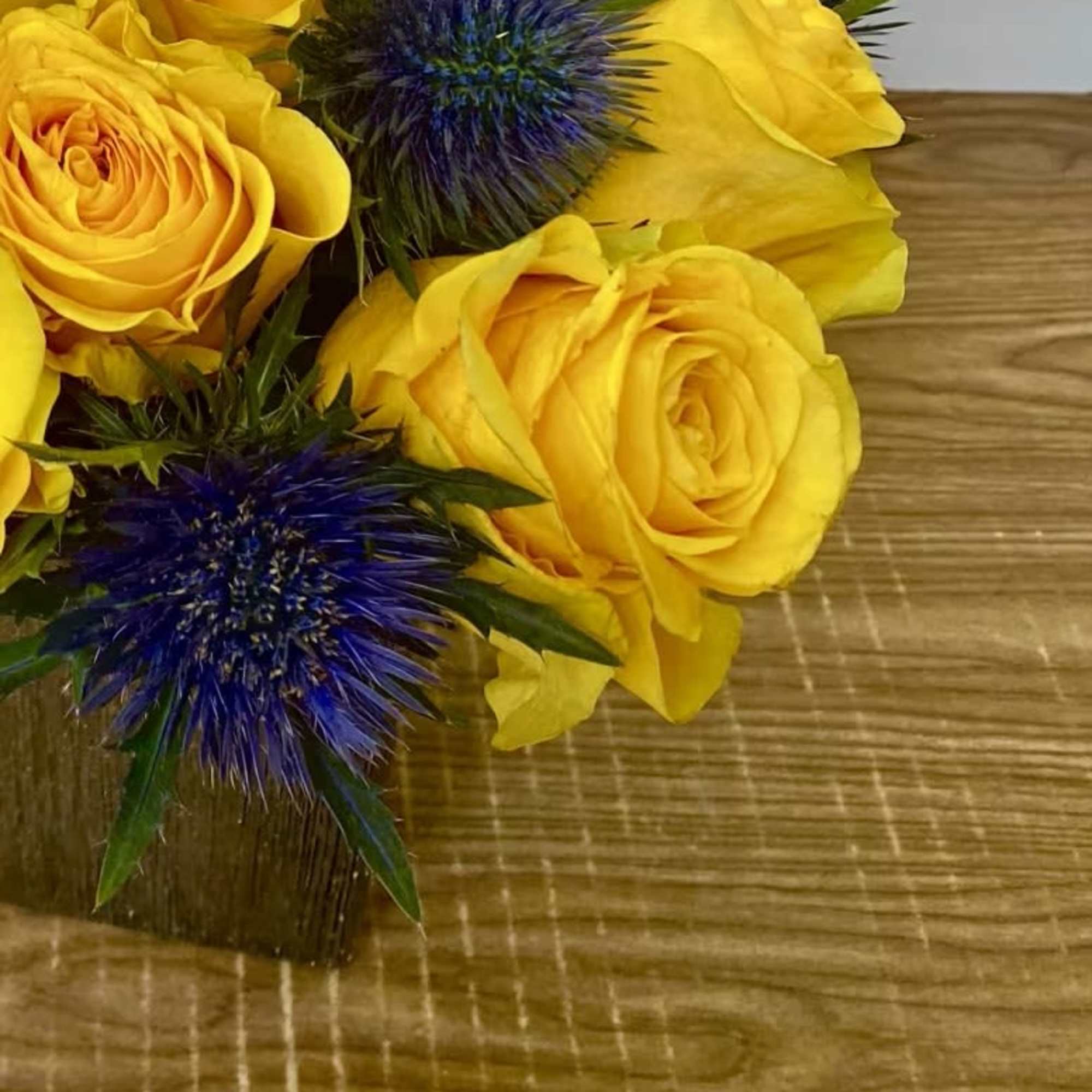 Yellow roses with blue thistle flowers on a wooden surface
