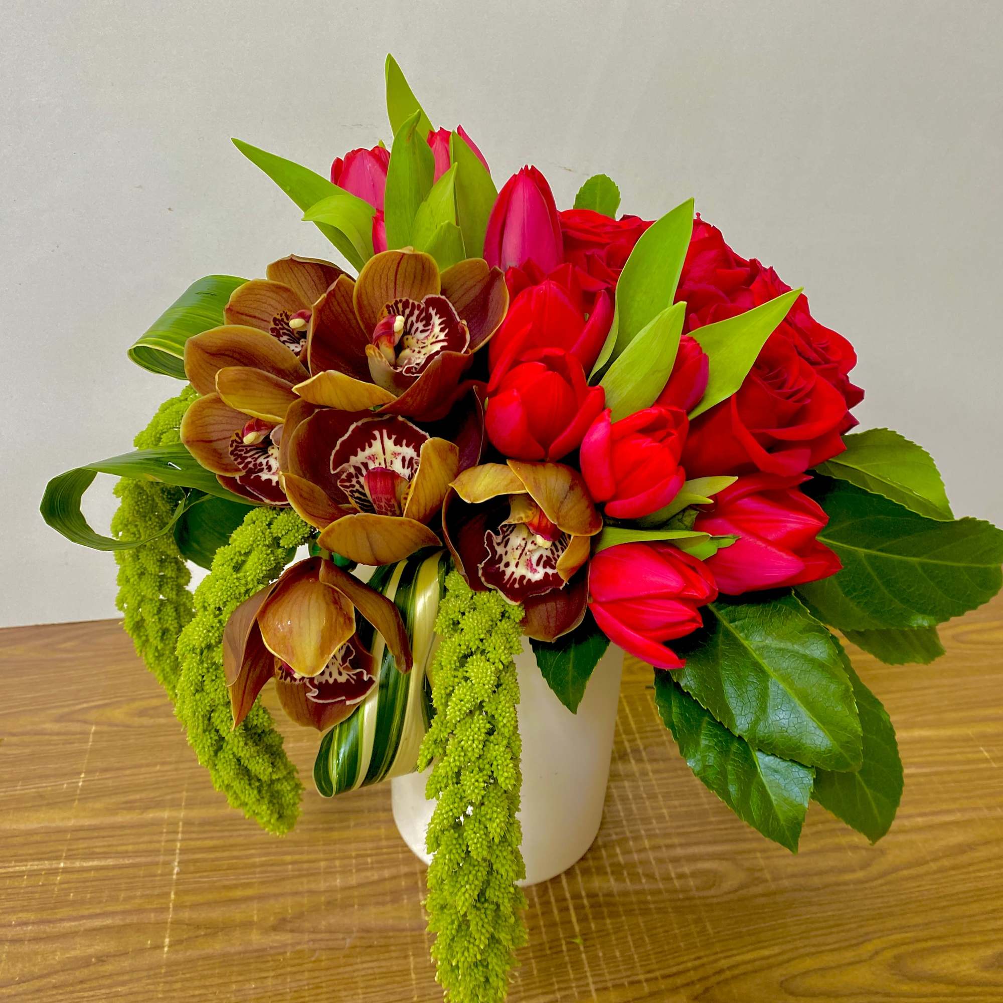 Bouquet of red tulips and brown orchids in a white vase