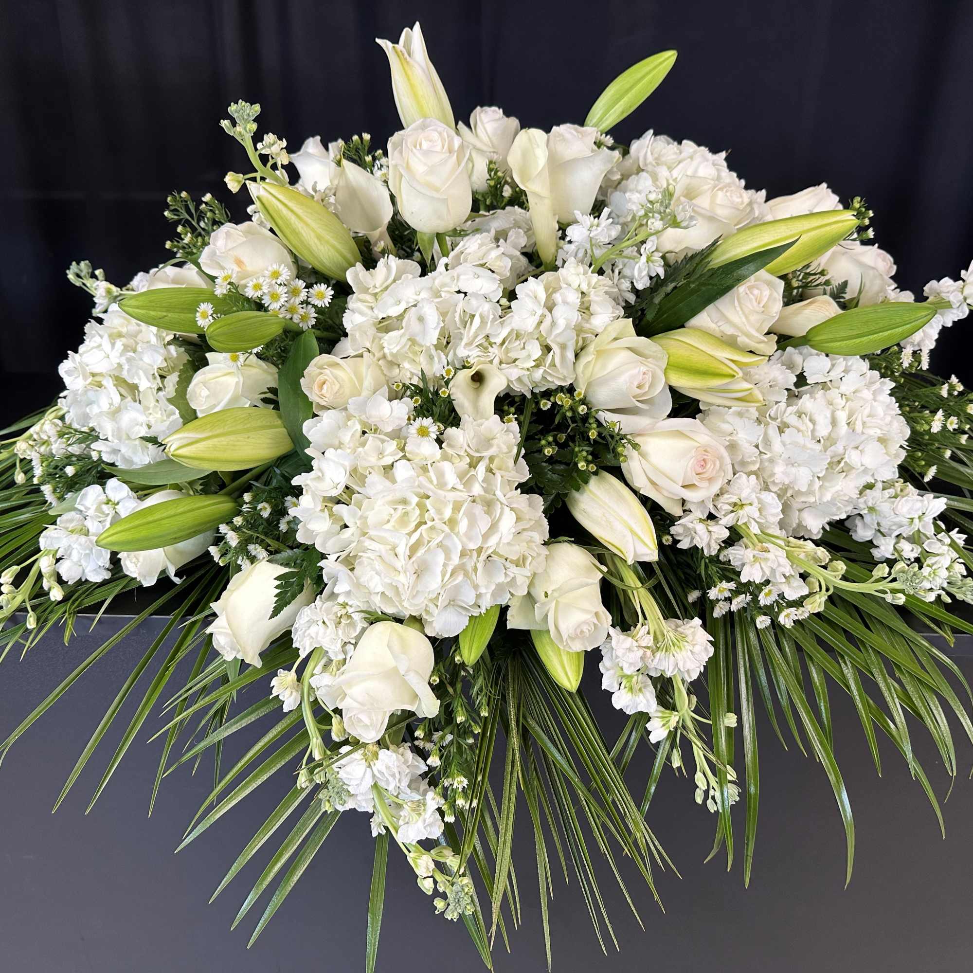 White floral casket spray with roses, lilies, and hydrangeas