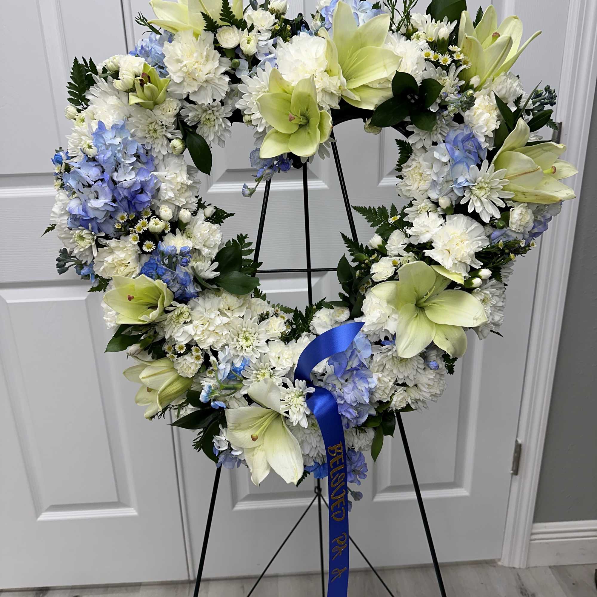 Heart-shaped floral wreath on a stand with white, blue, and pale yellow flowers
