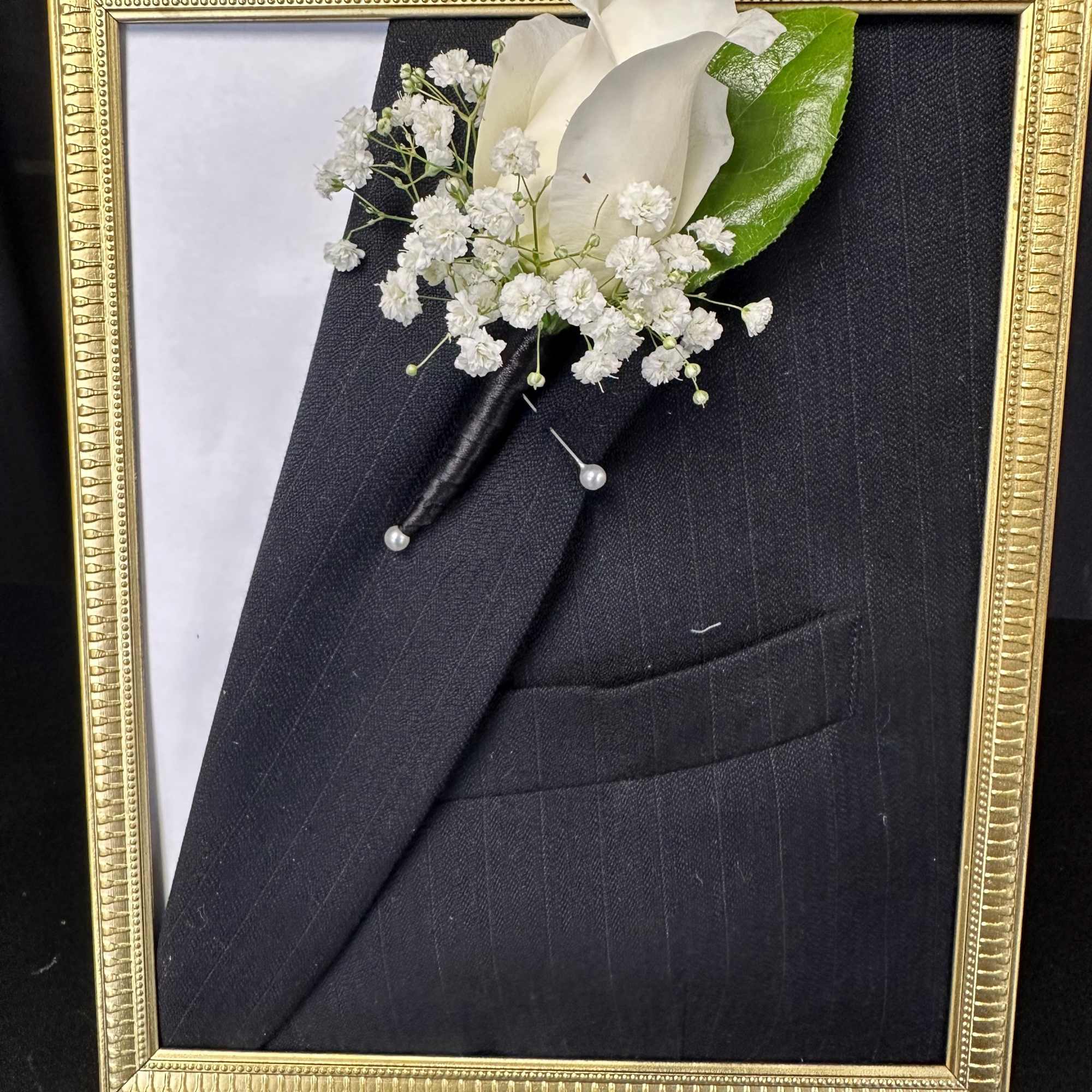 White boutonniere pinned to a black suit in a gold frame
