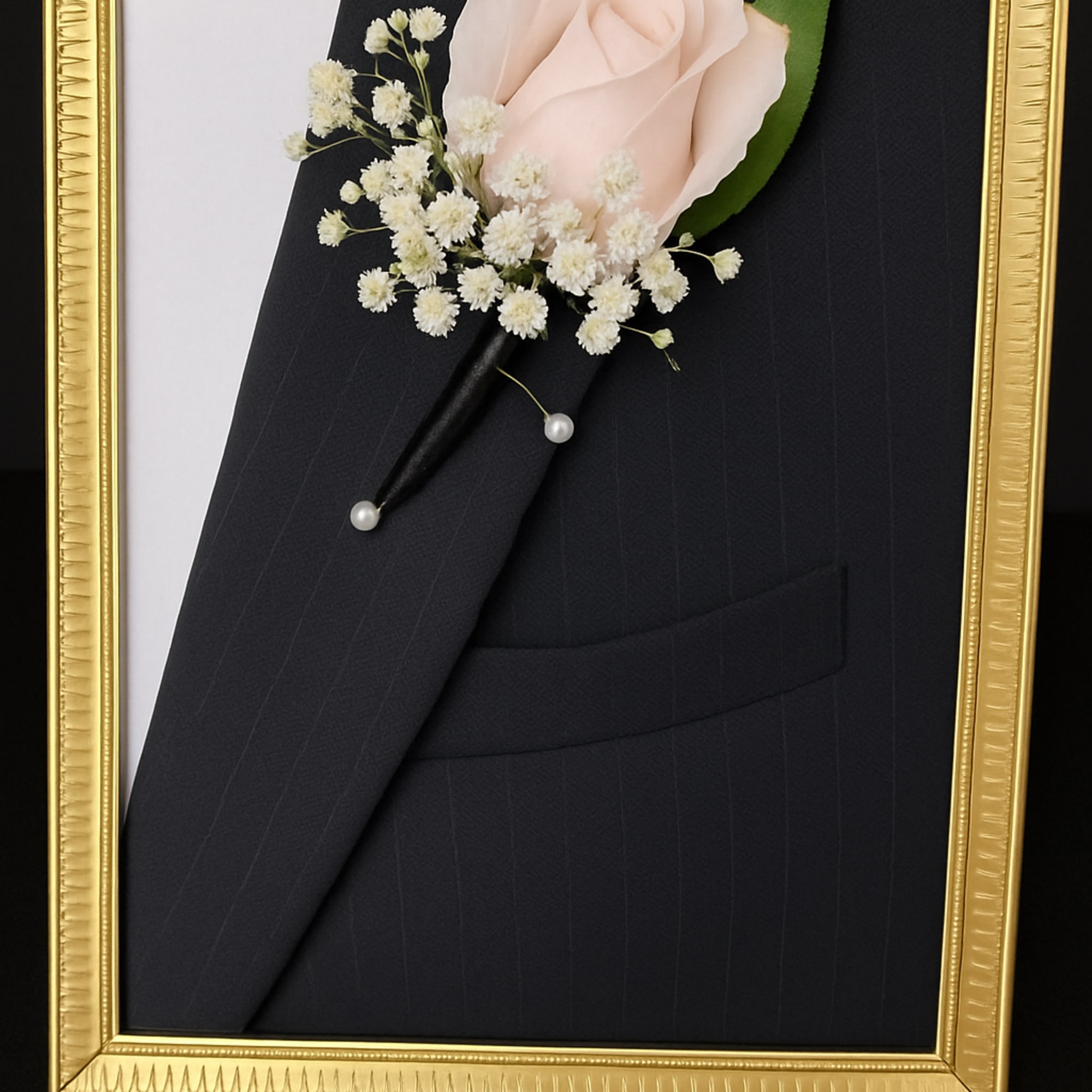 Boutonniere with a pale pink rose and white baby's breath in a gold frame