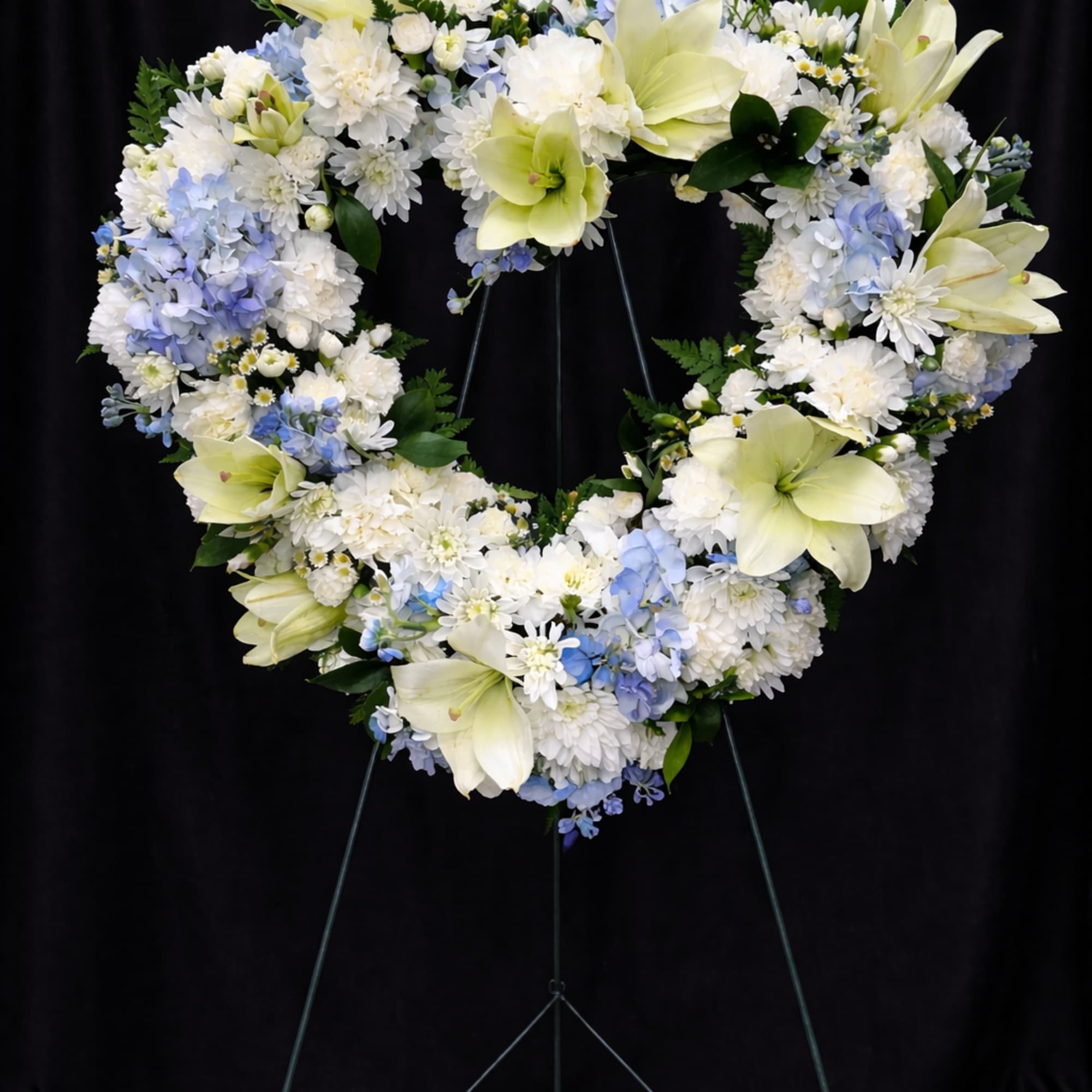 Heart-shaped floral wreath with white and pale blue flowers on a stand