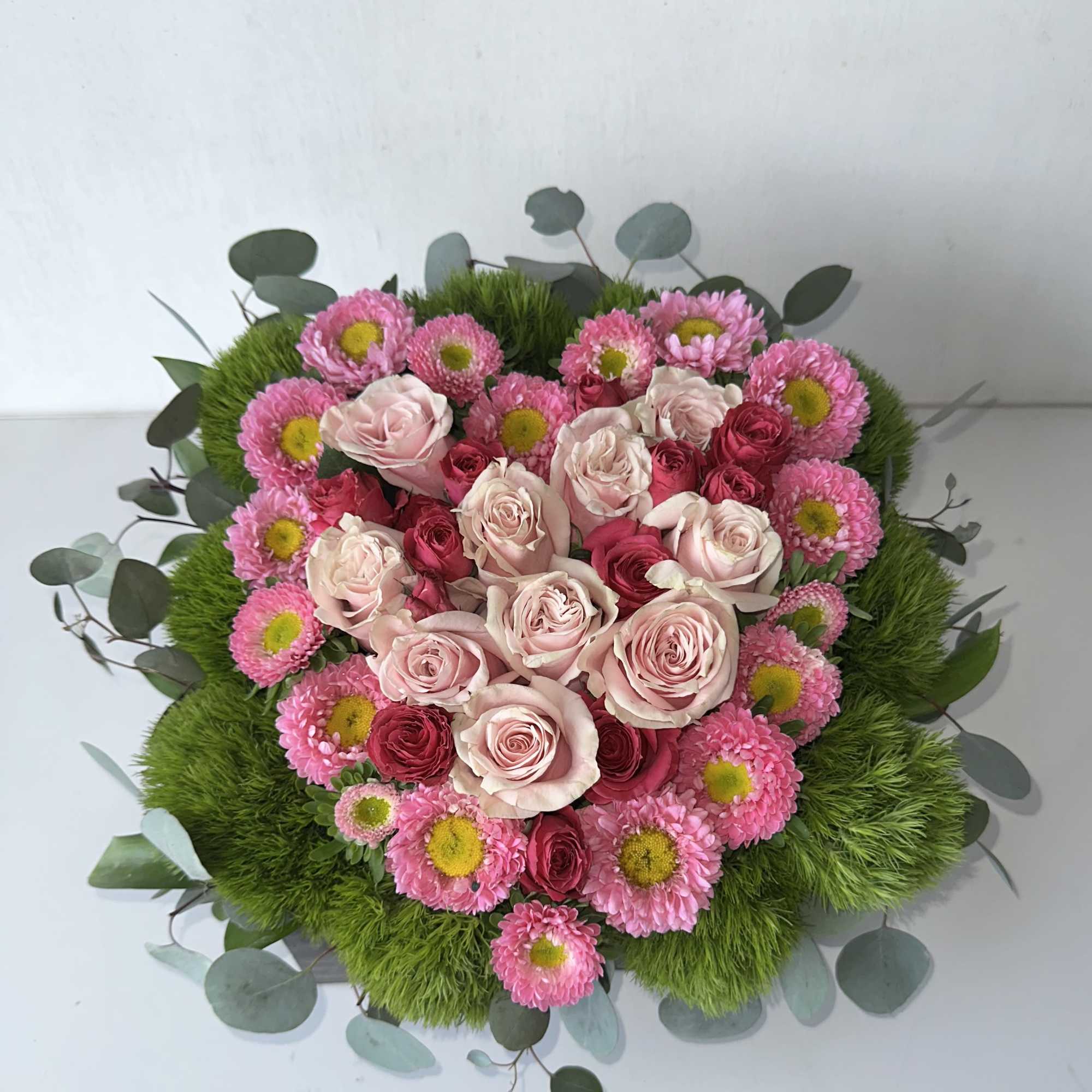 A heart-shaped floral design in a wooden box, created with fresh flowers