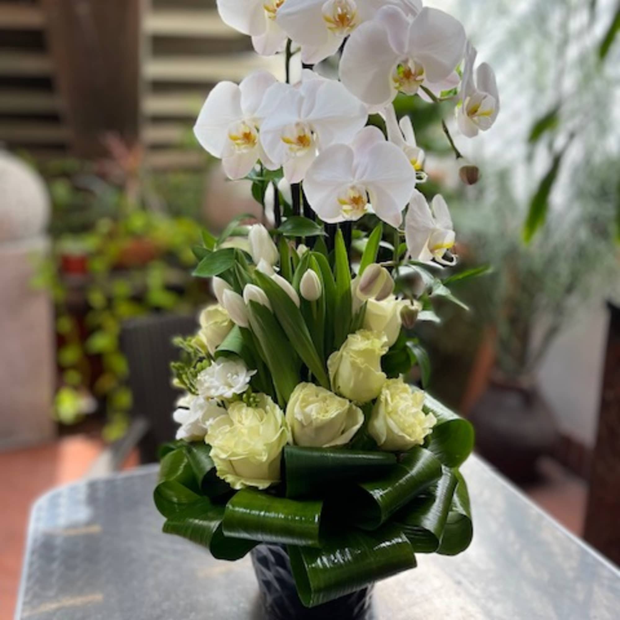 White orchids and pale roses in a black vase with green ribbon