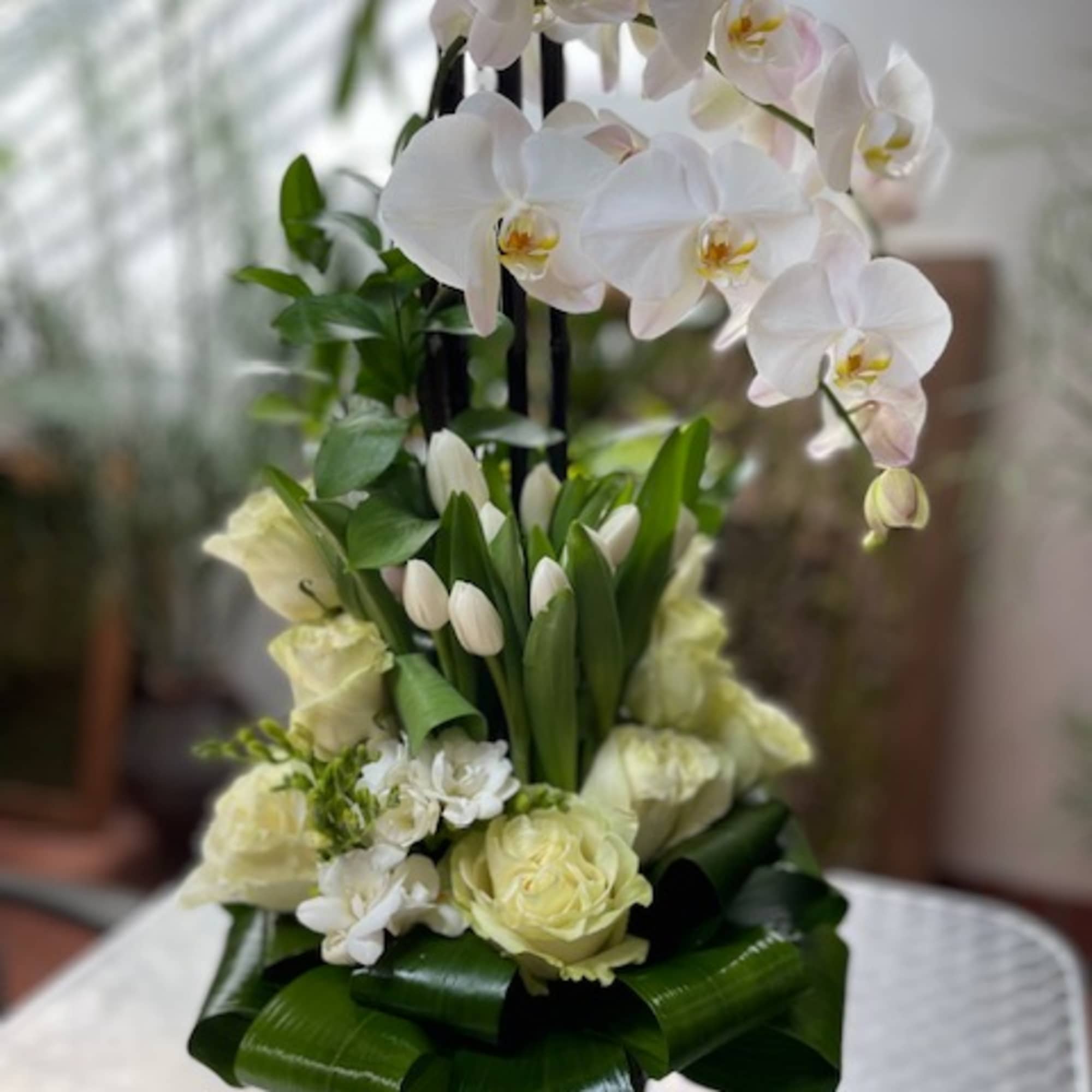 White orchids and pale roses arranged in a tall black vase