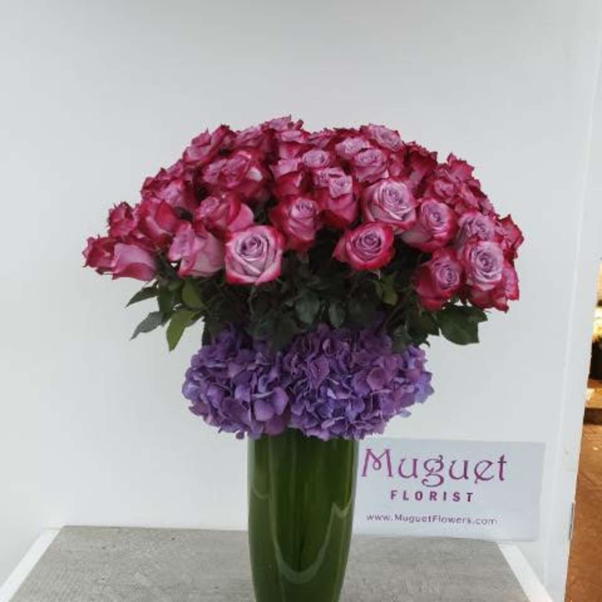 Pink roses and purple hydrangeas arranged in a tall green vase