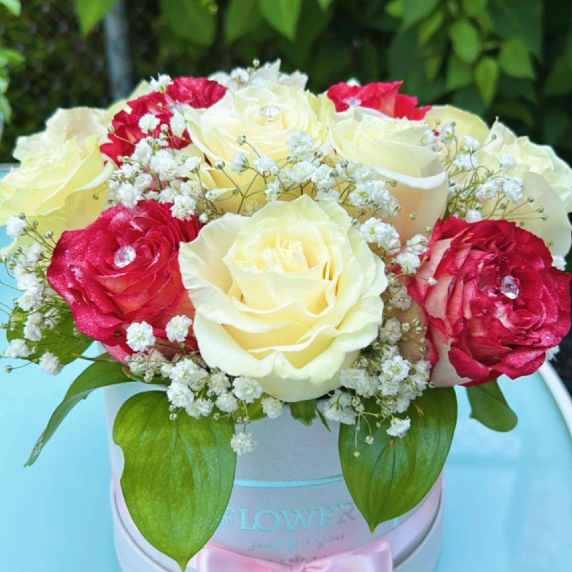 Red and cream roses arranged in a round hat box with baby's breath