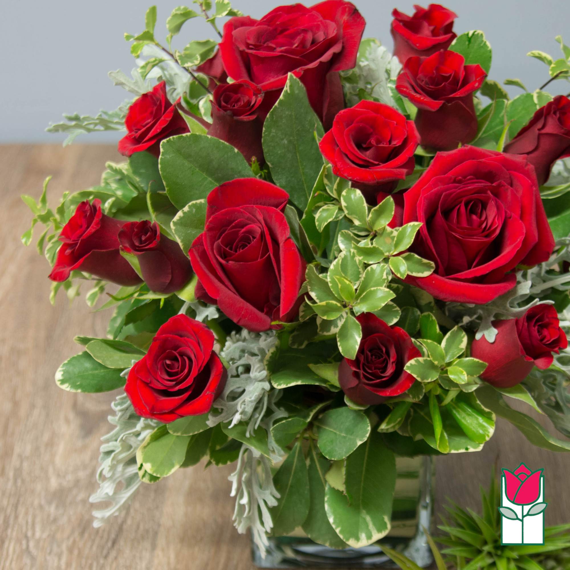 Red roses arranged in a clear glass vase with mixed greenery