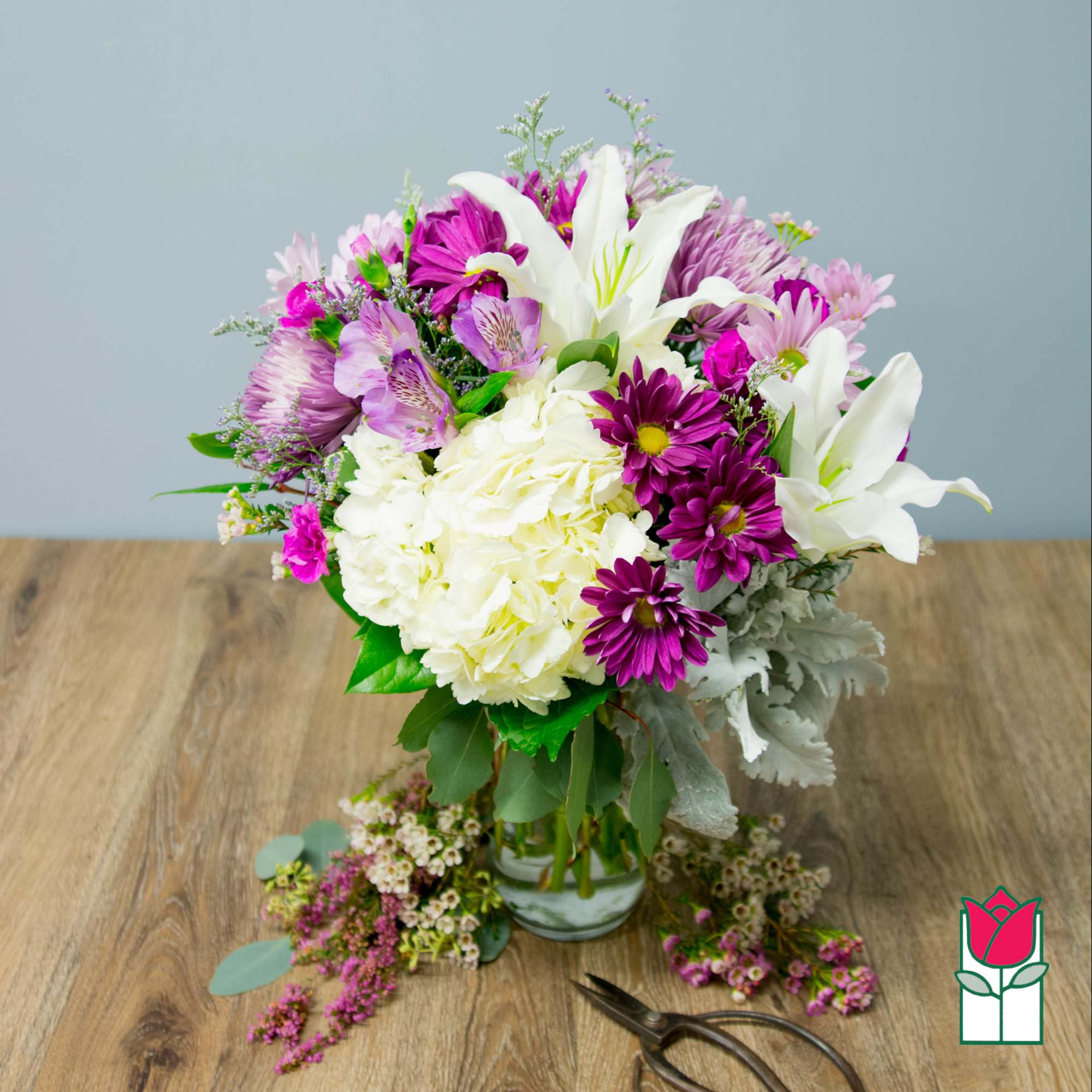 Mixed bouquet of white lilies, purple daisies, and pink flowers in a glass vase