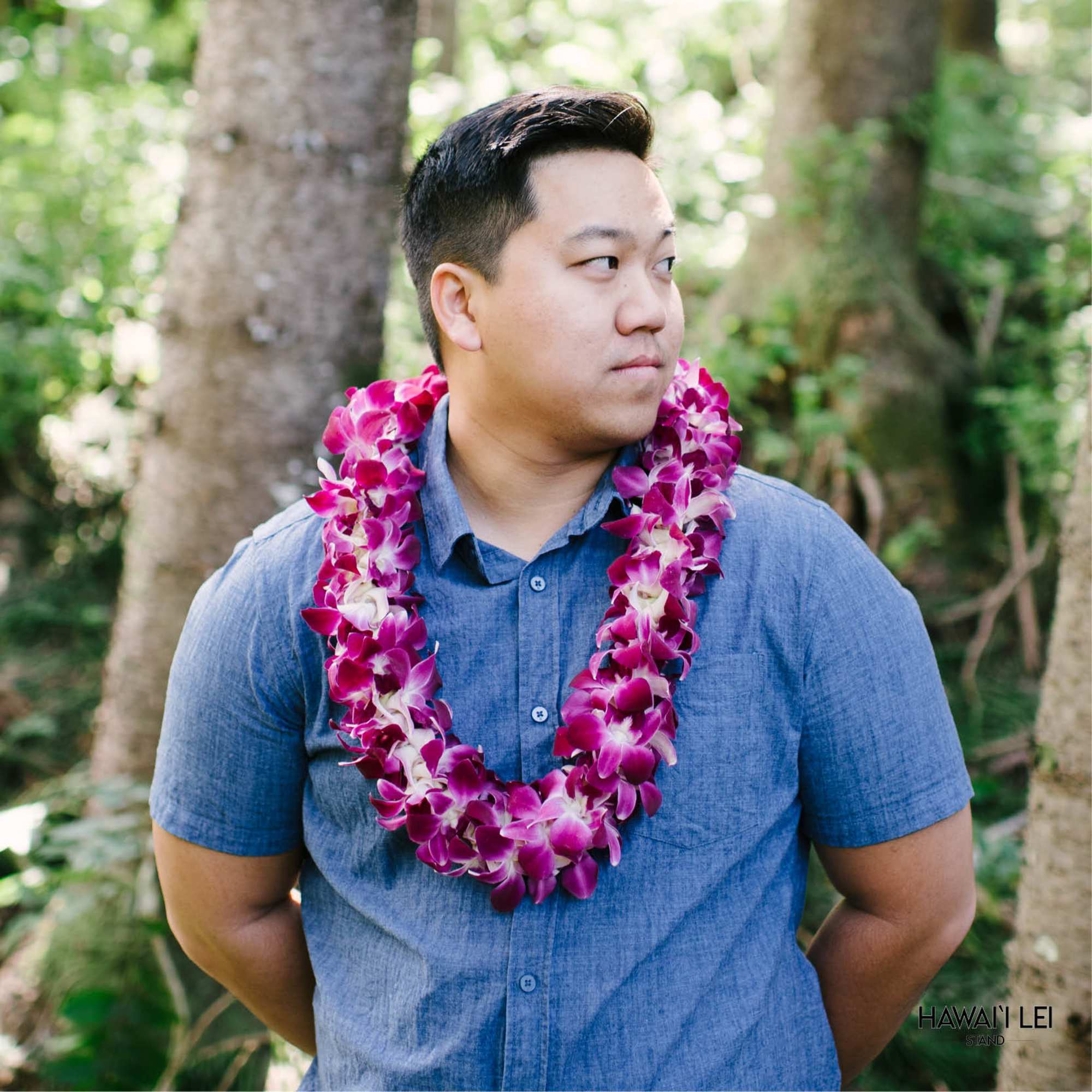 Purple and white orchid lei worn around a person's neck outdoors