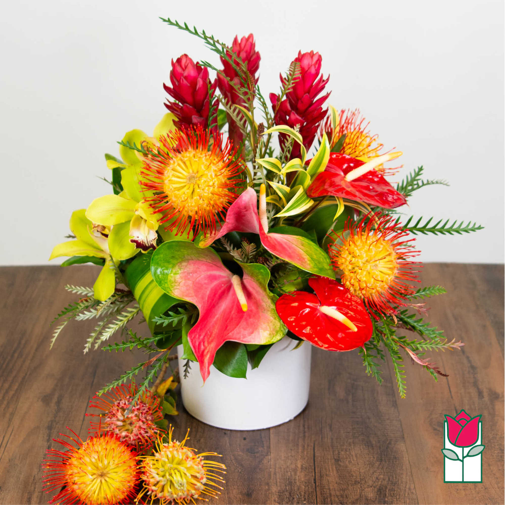 Tropical bouquet with red anthuriums and yellow pincushion blooms in a white vase