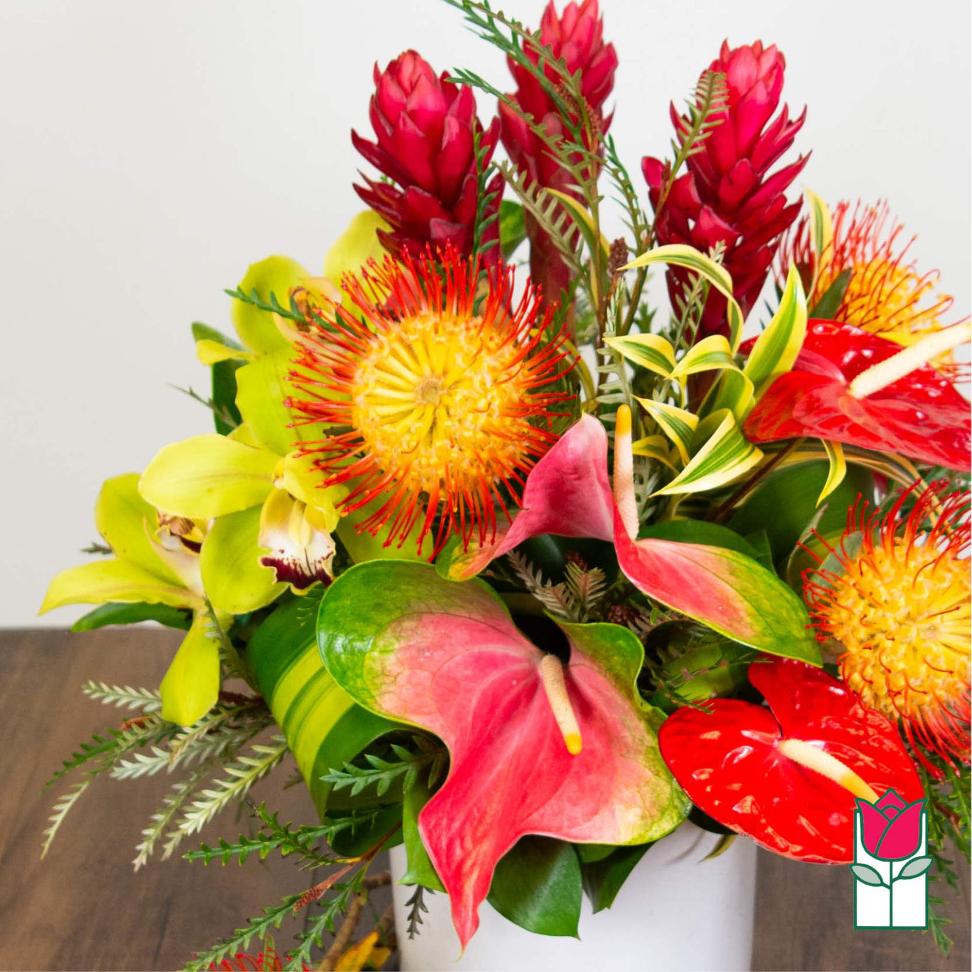 Tropical bouquet with red anthuriums, yellow orchids, and spiky red-orange blooms in a white vase