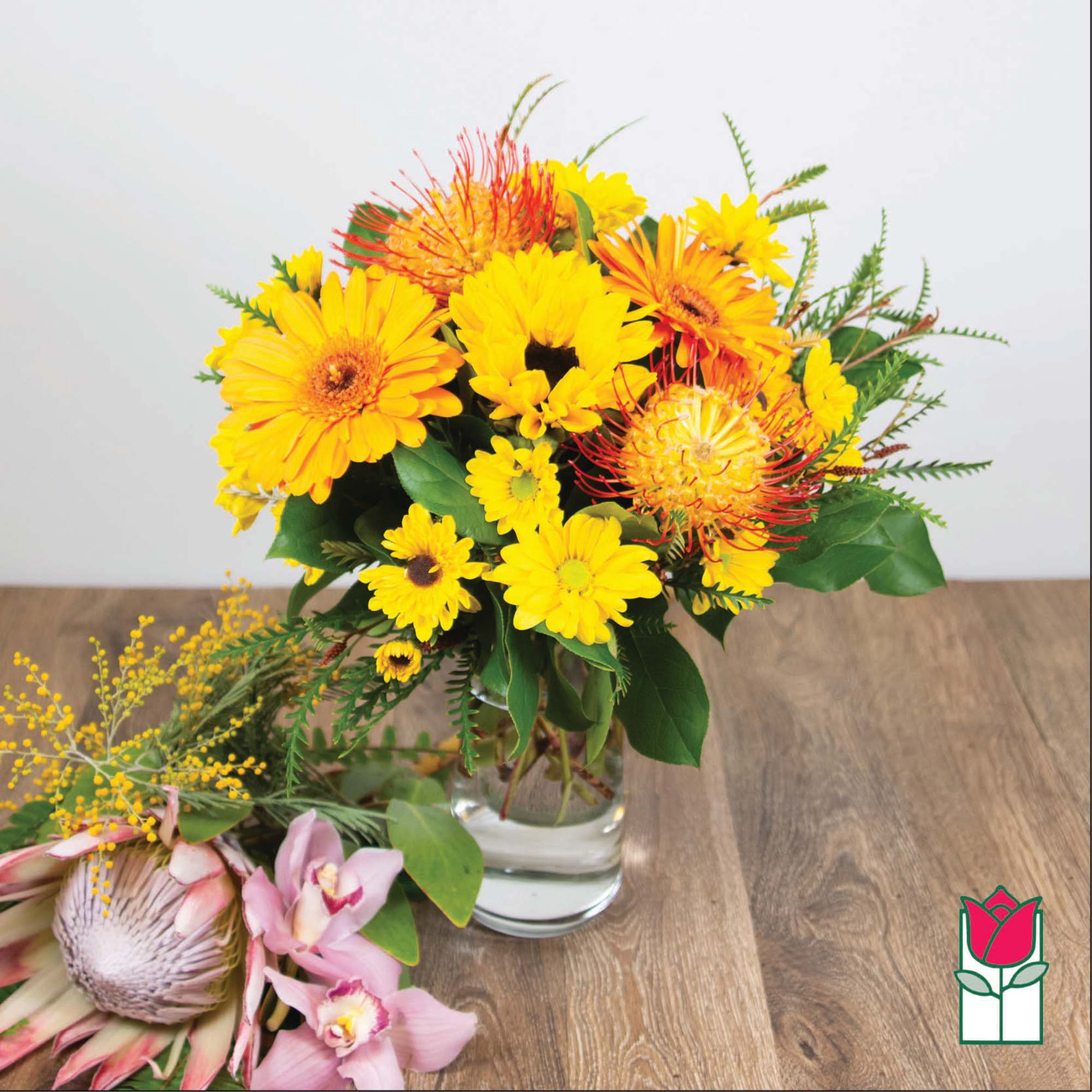 Yellow and orange mixed bouquet in a clear glass vase with pink orchids beside it