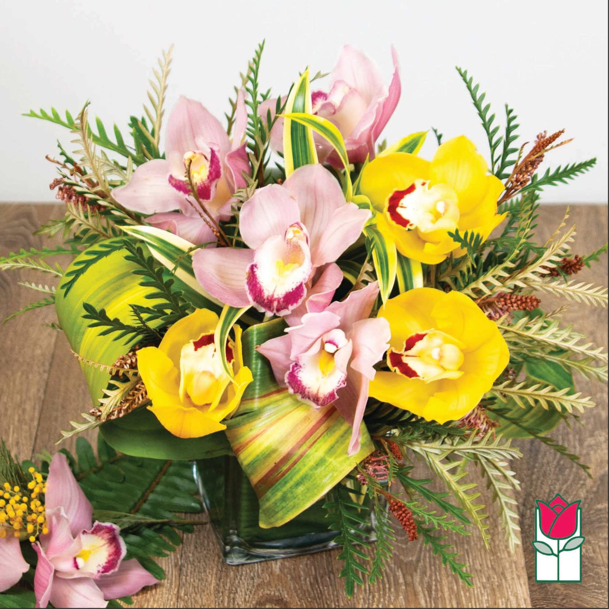 Pink and yellow orchids in a glass vase with tropical leaves