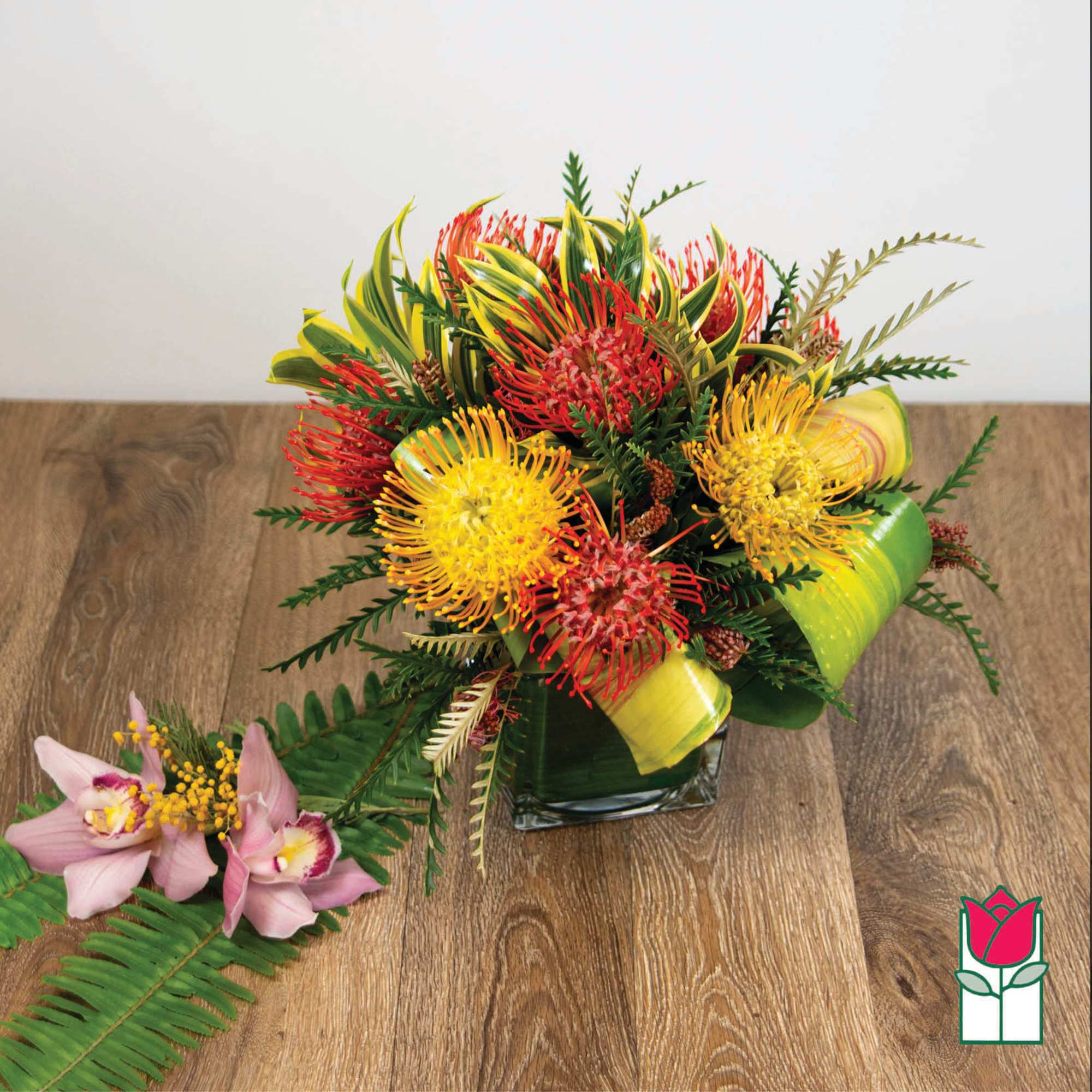 Tropical bouquet with red and yellow pincushion flowers in a square vase