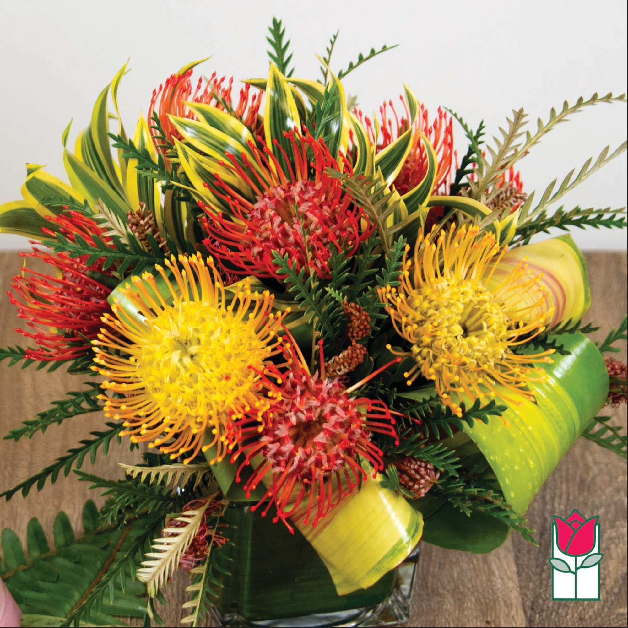 Bright tropical bouquet with red and yellow pincushion blooms in a glass vase