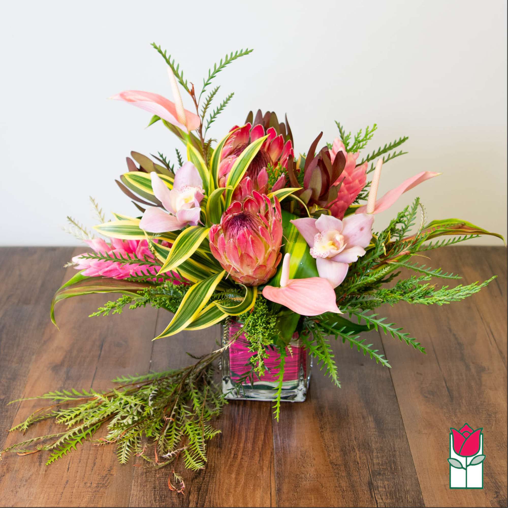 Tropical bouquet with pink protea and orchids in a square glass vase