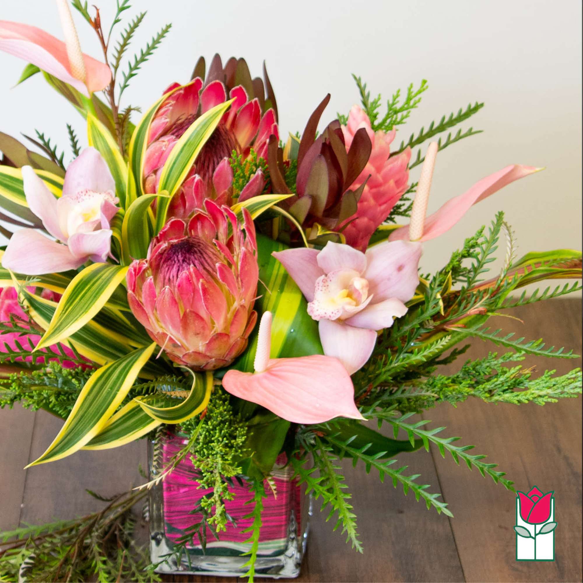 Pink protea and orchids in a square glass vase