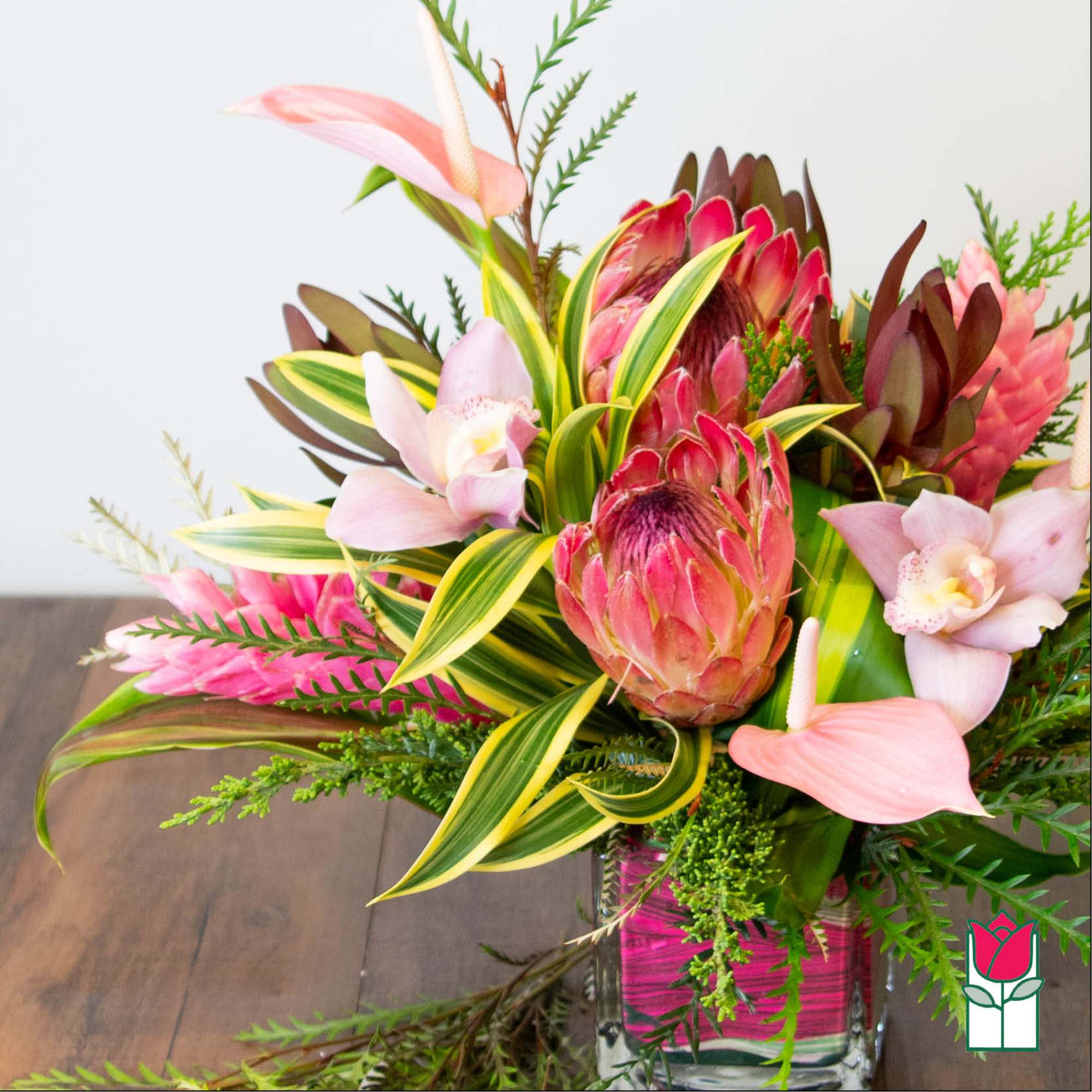 Tropical bouquet with pink protea and orchids in a glass vase