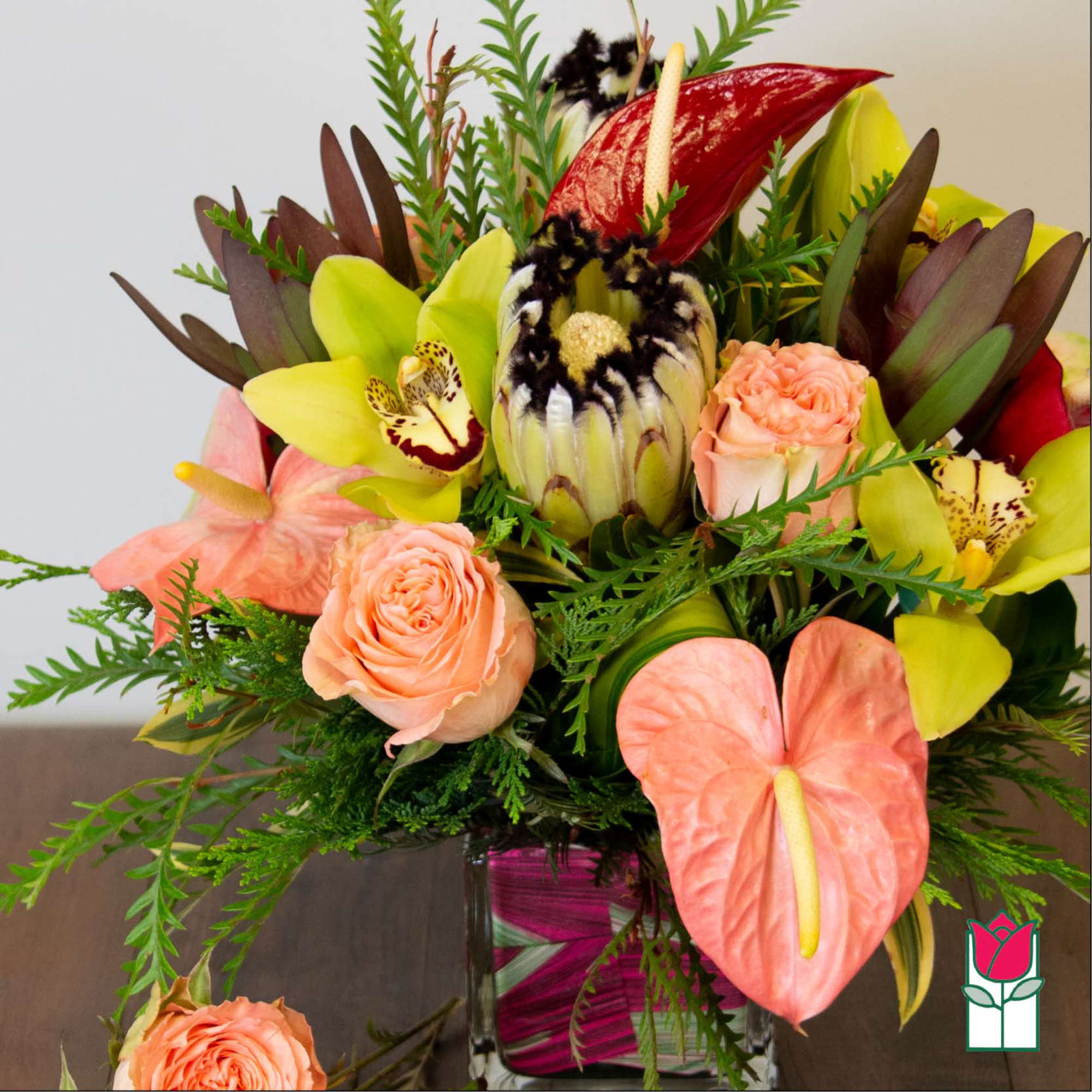 Tropical bouquet with peach roses and yellow orchids in a glass vase