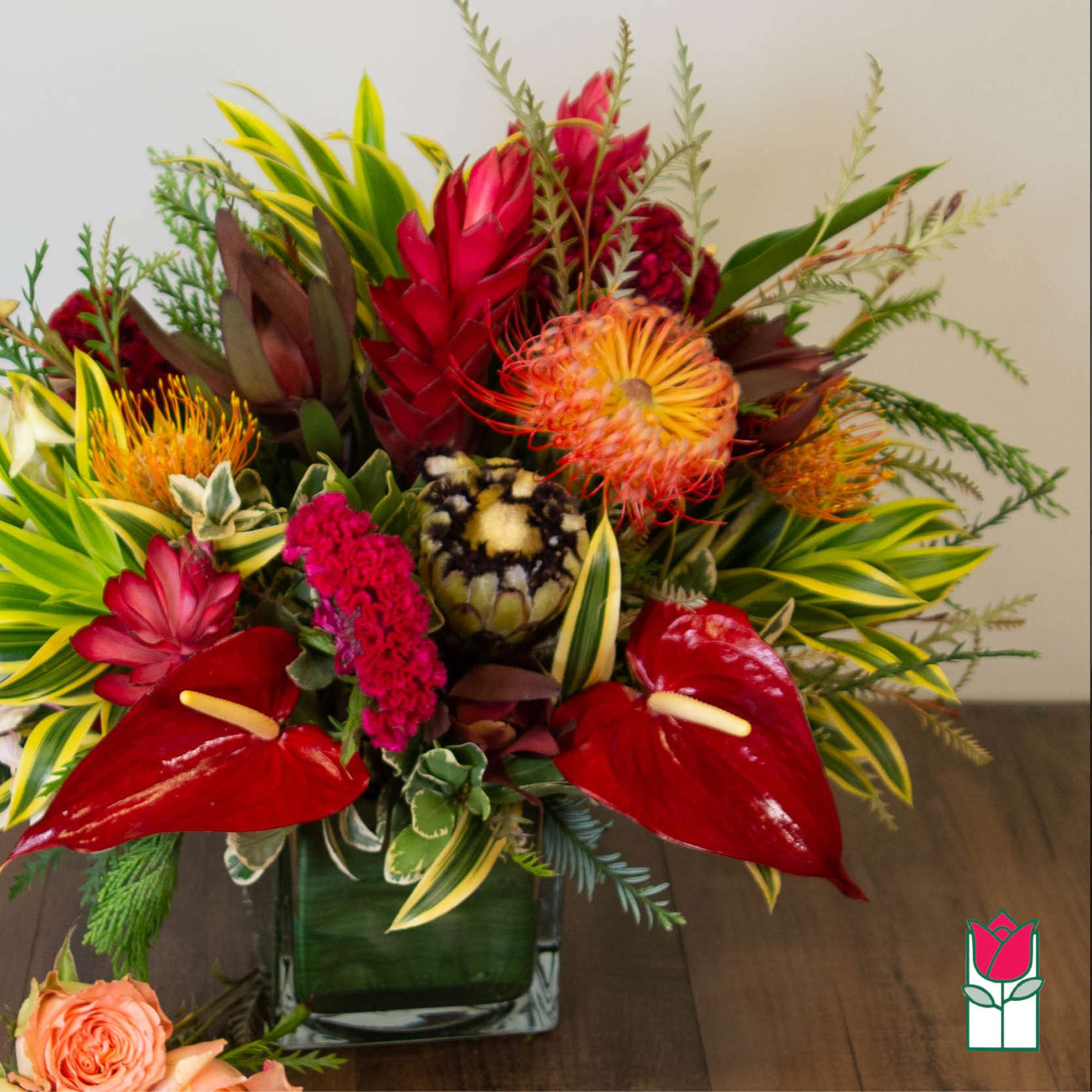 Tropical flower arrangement in a square glass vase with red anthuriums and orange blooms