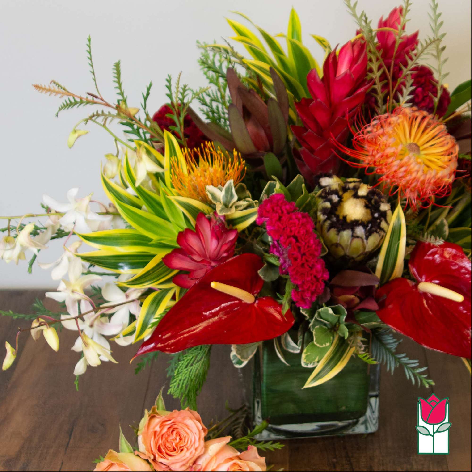 Tropical flower arrangement in a square glass vase with red, orange, and white blooms