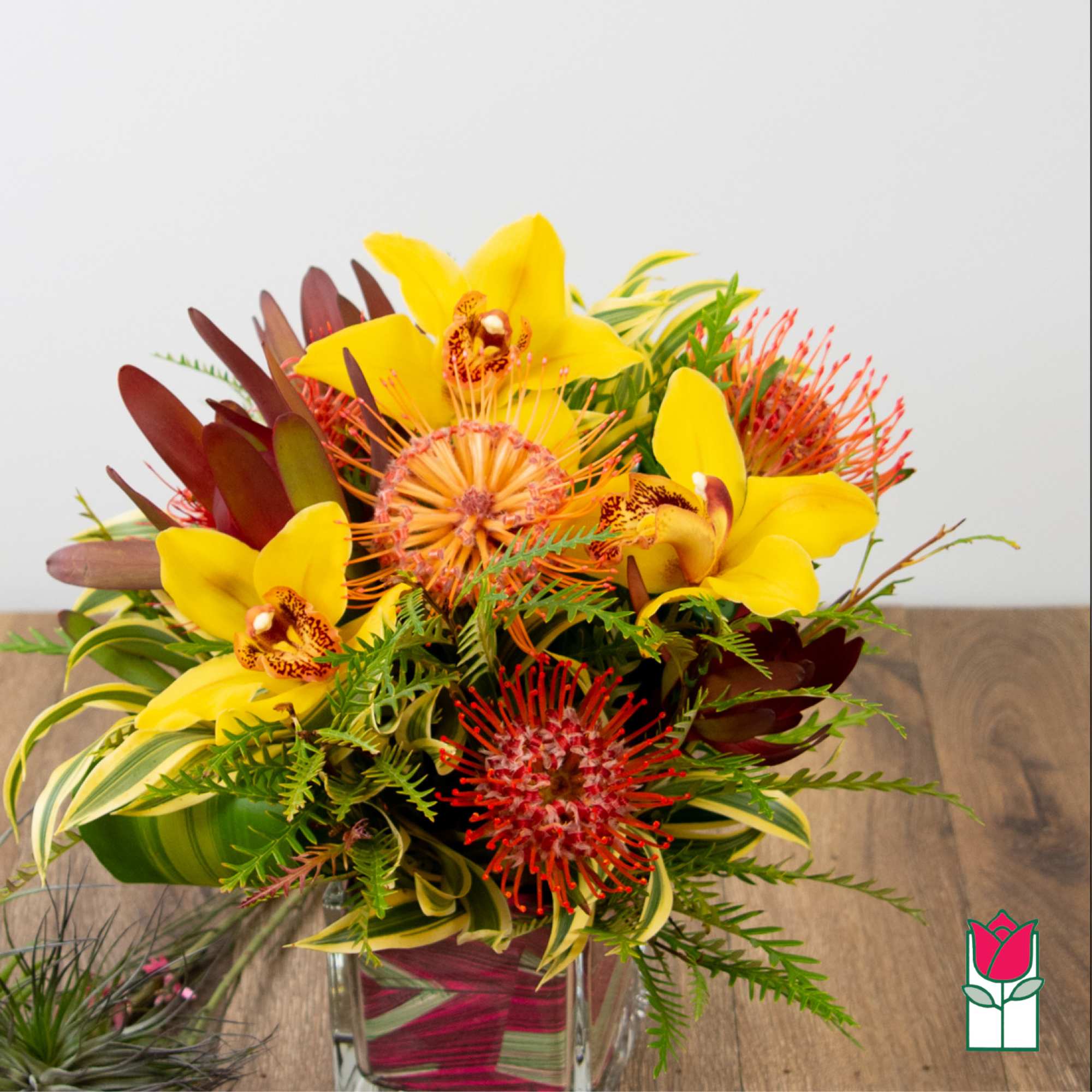 Tropical bouquet with yellow orchids and red pincushion protea in a glass vase