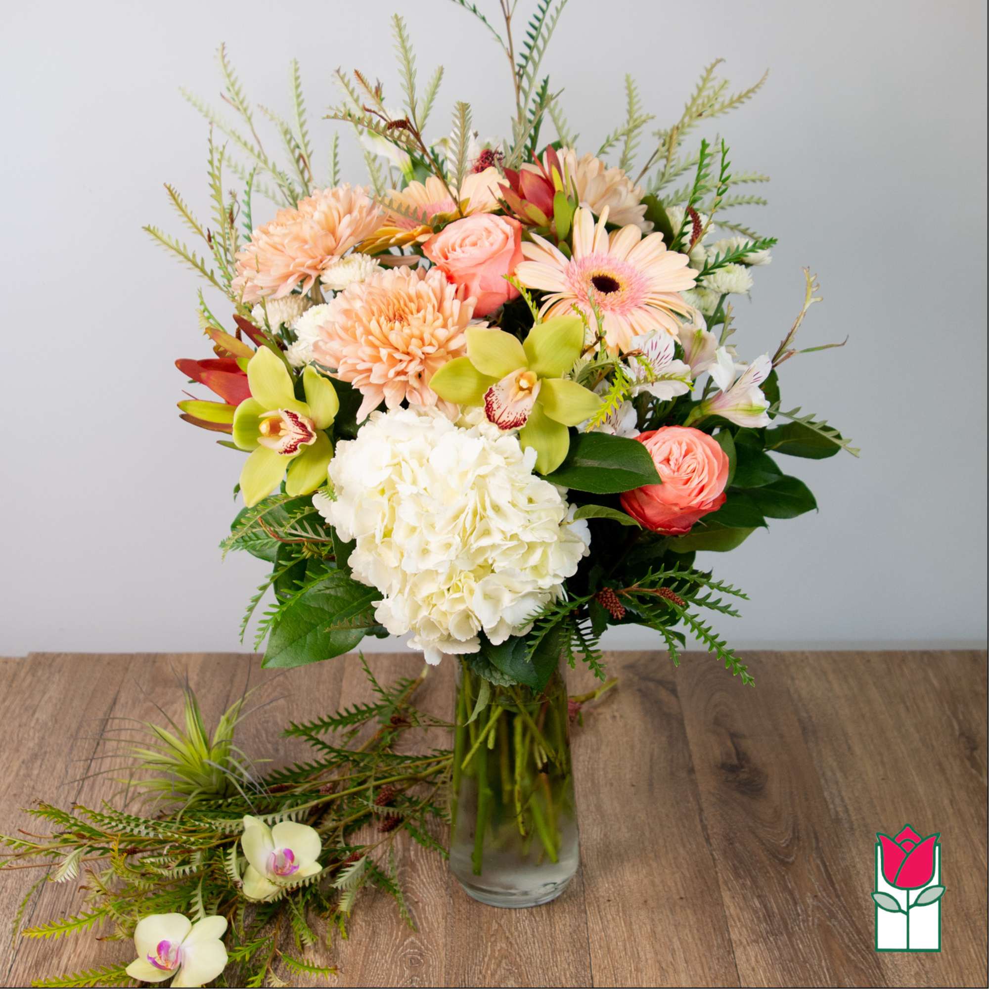 Mixed bouquet of peach, white, and green flowers in a glass vase
