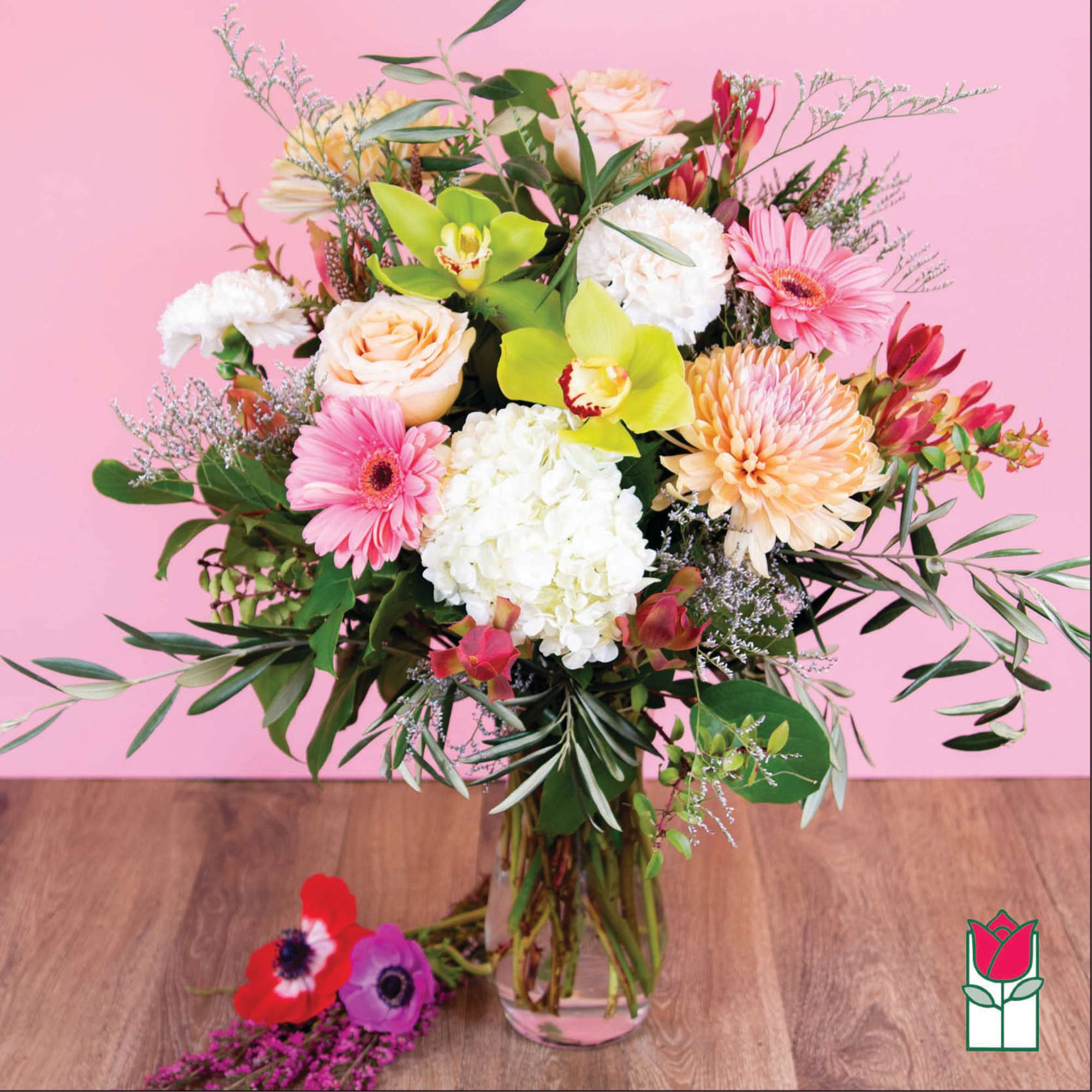 Mixed bouquet of pink, white, peach, and green flowers in a glass vase.