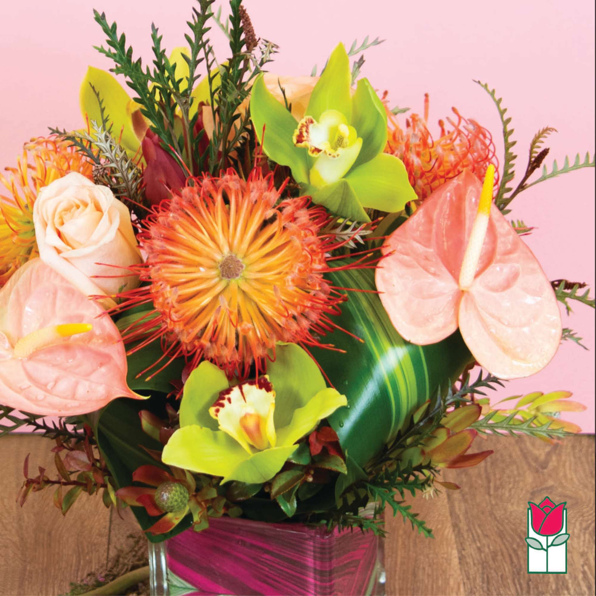 Tropical bouquet with anthuriums, orchids, and spiky orange blooms in a glass vase