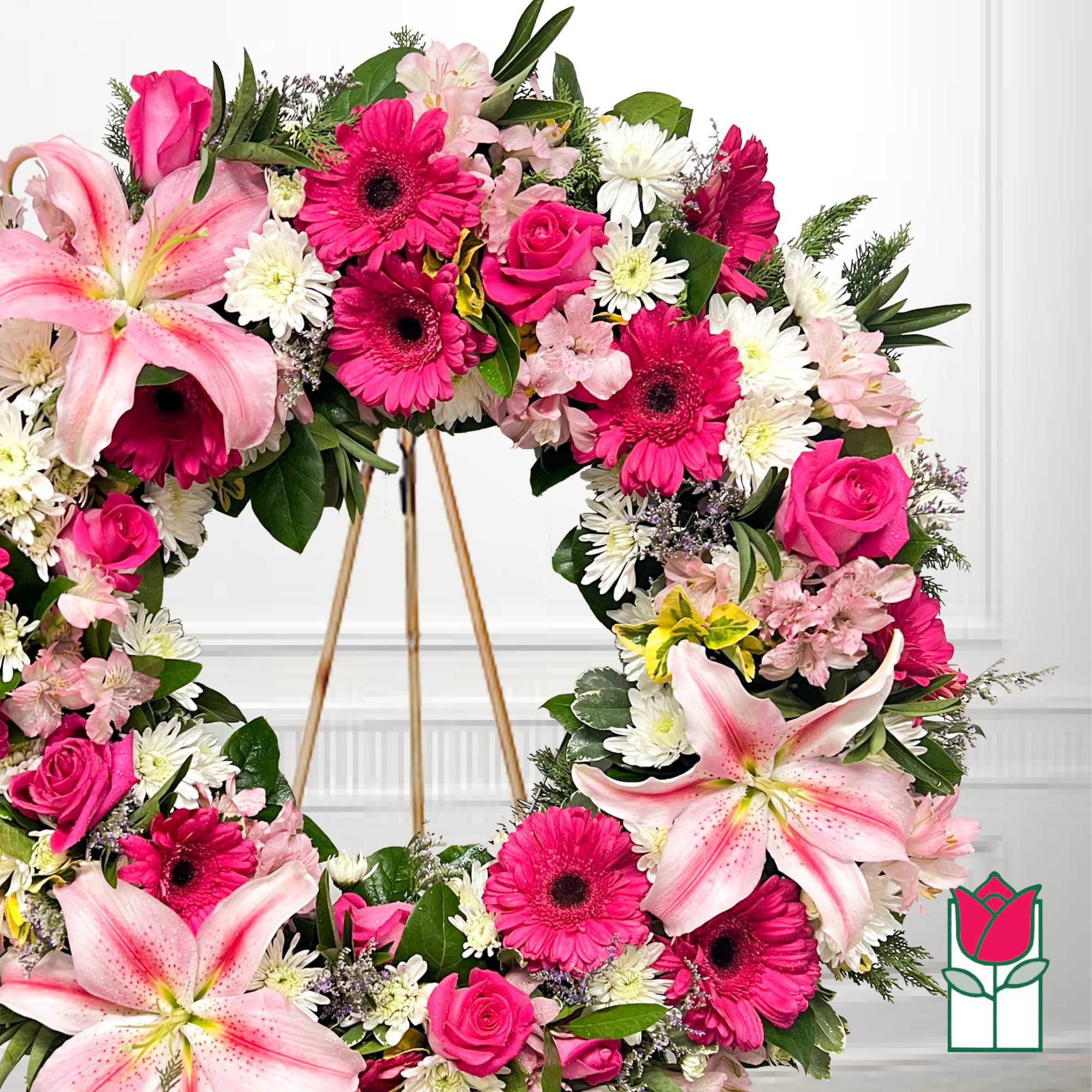 Pink and white floral wreath with lilies, roses, and daisies on a stand
