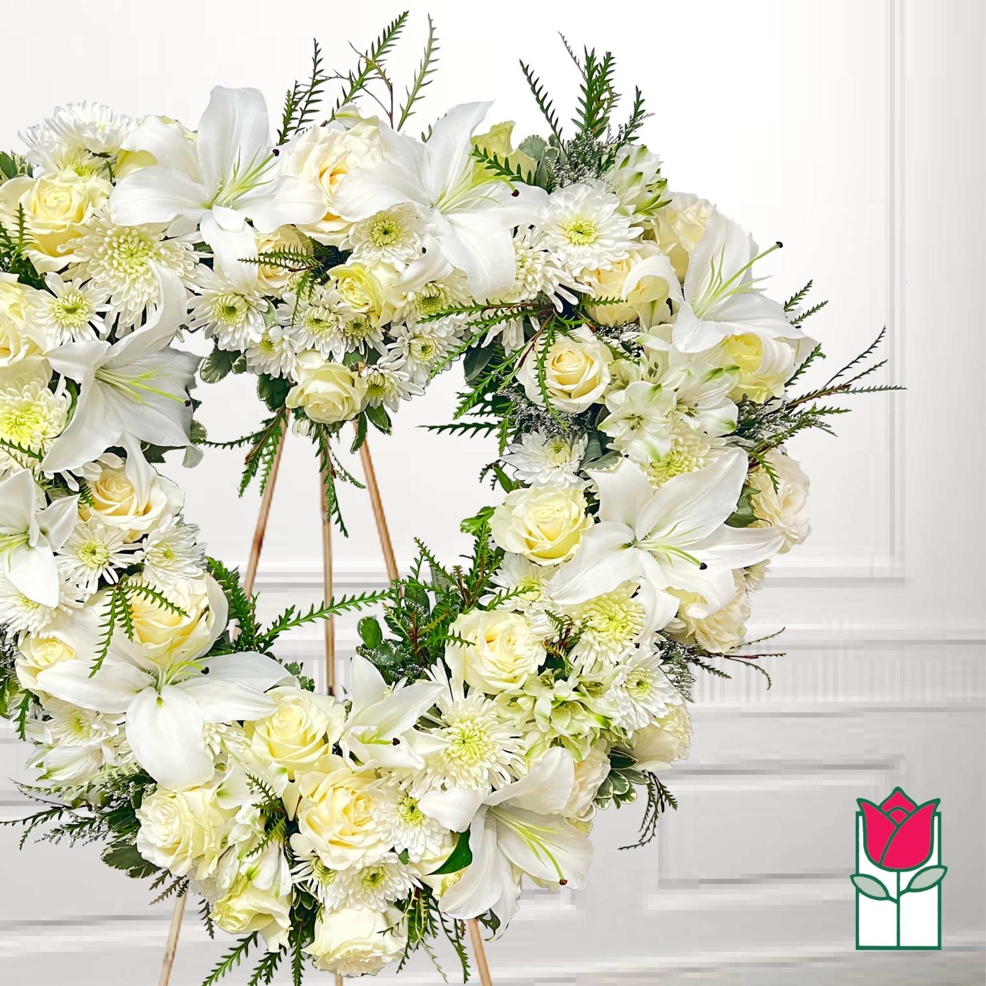 White floral wreath with lilies, roses, and daisies on a stand