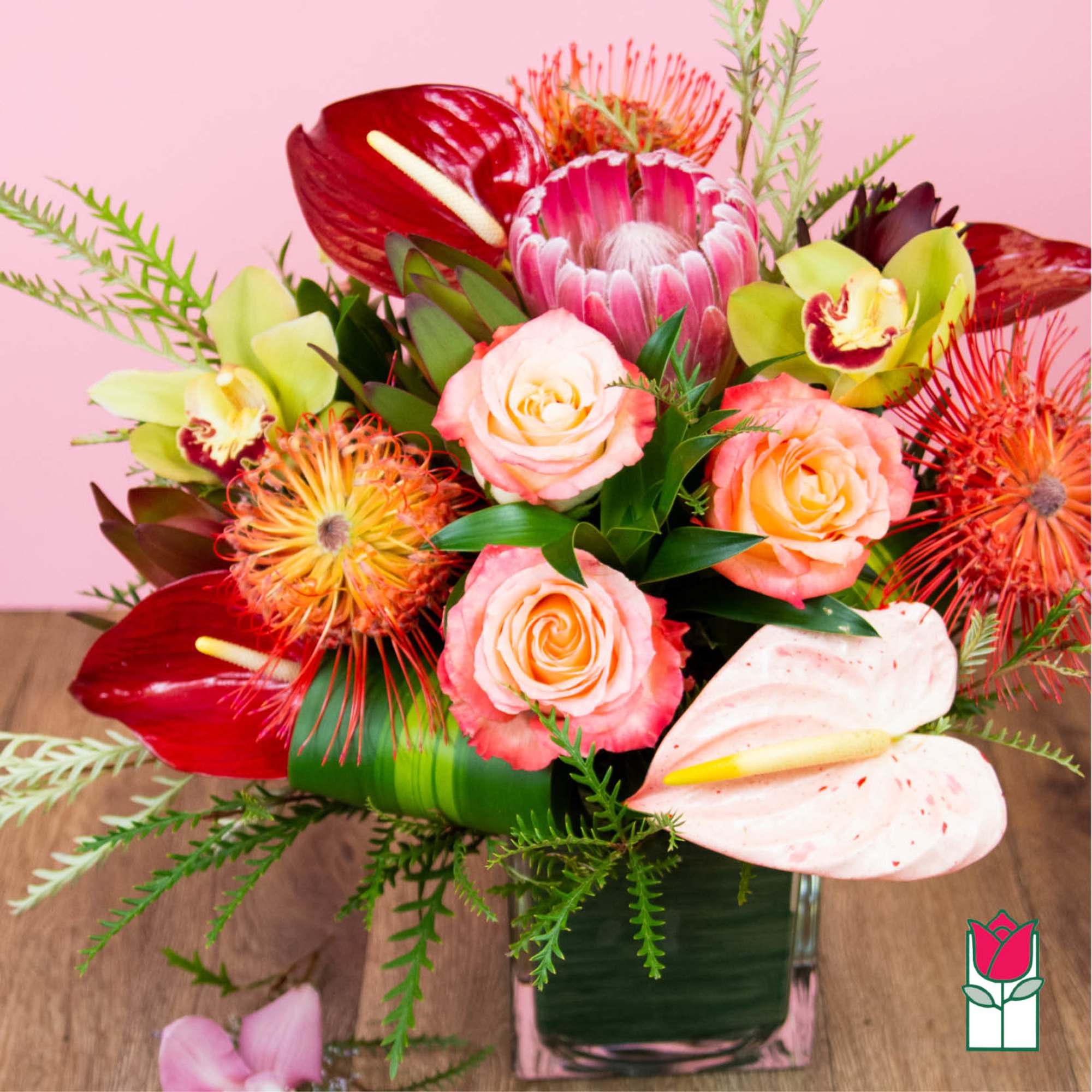Tropical bouquet with roses, anthuriums, and orchids in a glass vase
