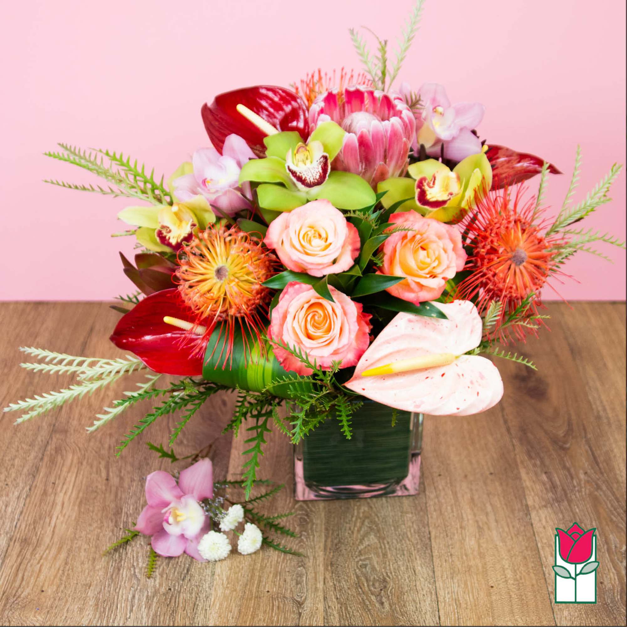 Mixed tropical bouquet in a square glass vase with pink and red blooms