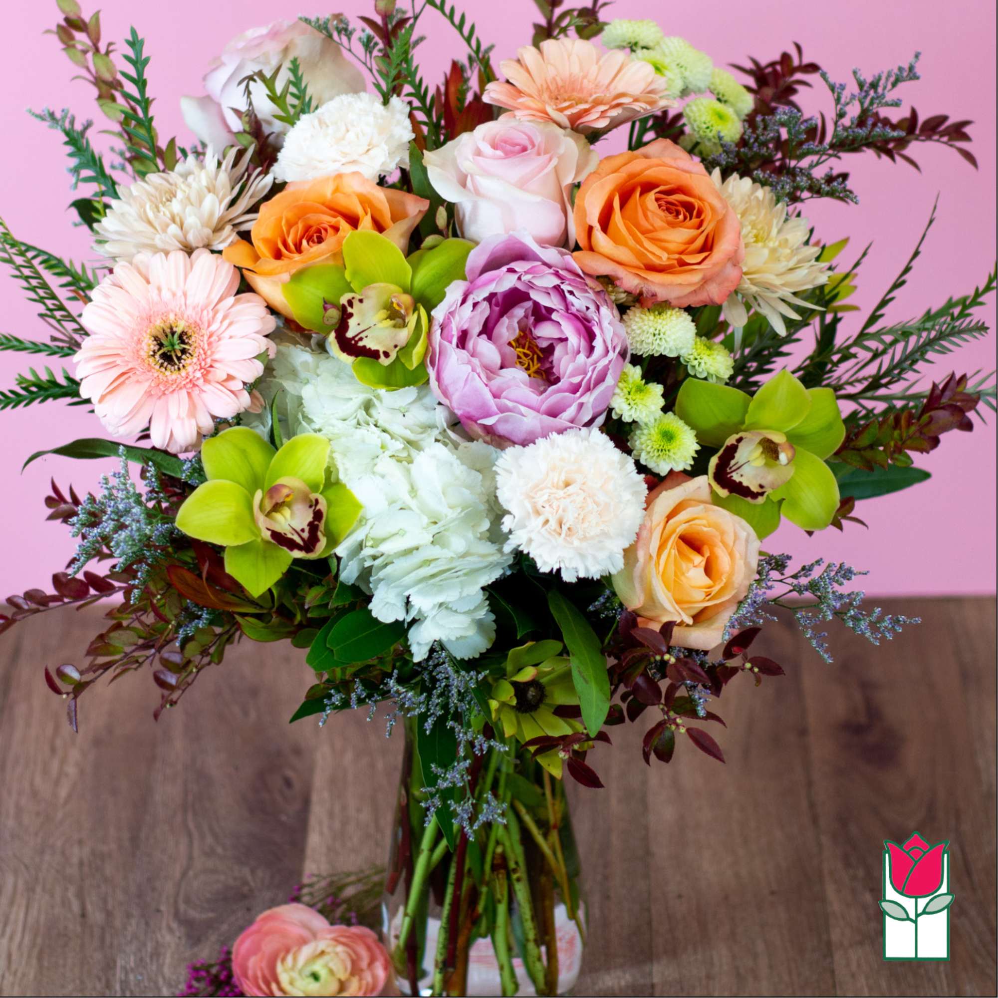 Mixed bouquet of roses, gerbera daisies, orchids, and peonies in a glass vase