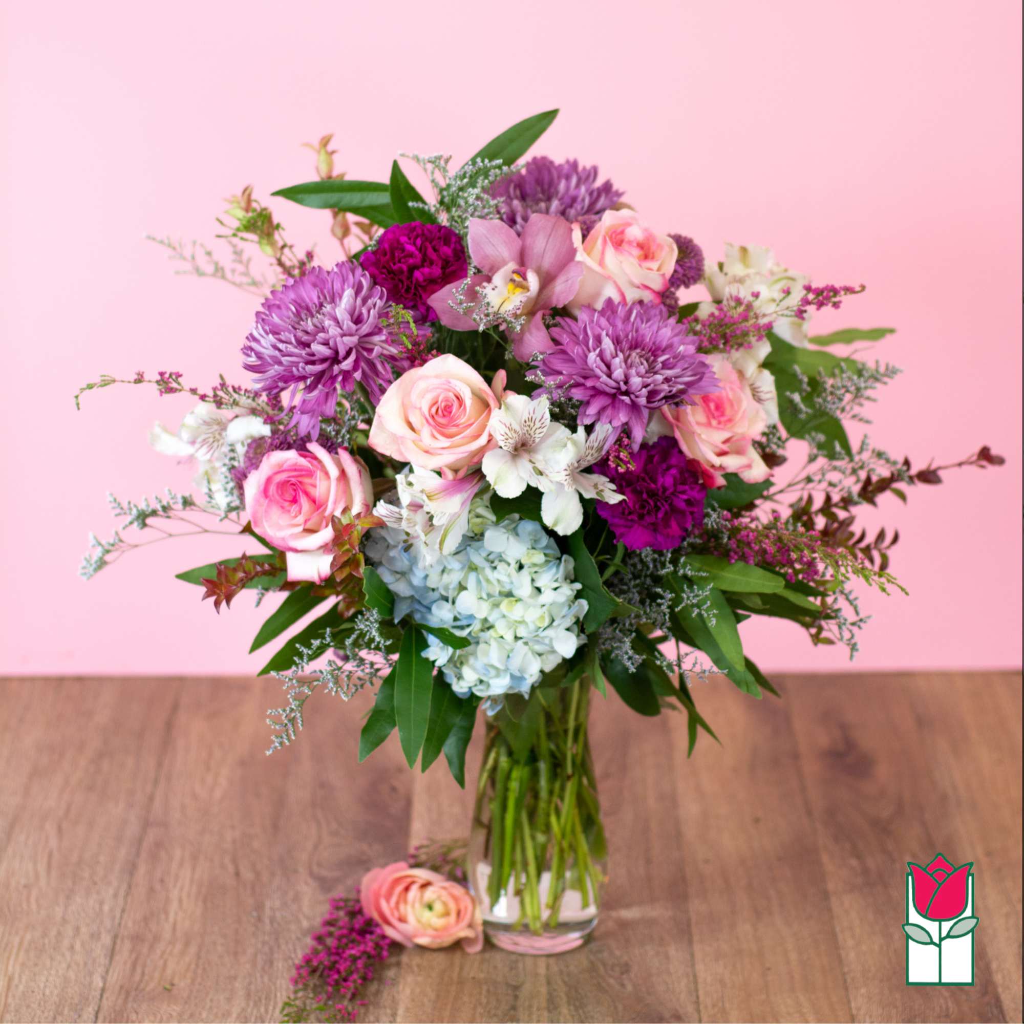 Tall mixed bouquet of pink roses, purple mums, blue hydrangea and white blooms in a clear glass vase