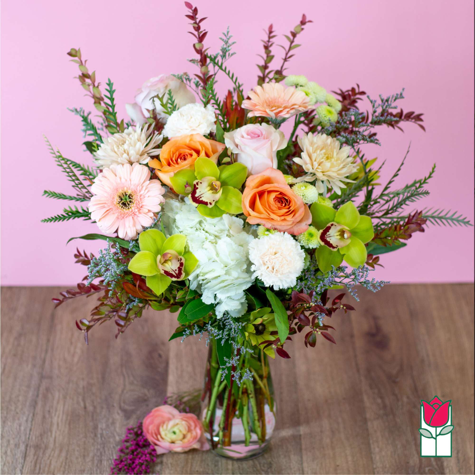 Mixed bouquet of roses, gerbera daisies, orchids, and white blooms in a glass vase